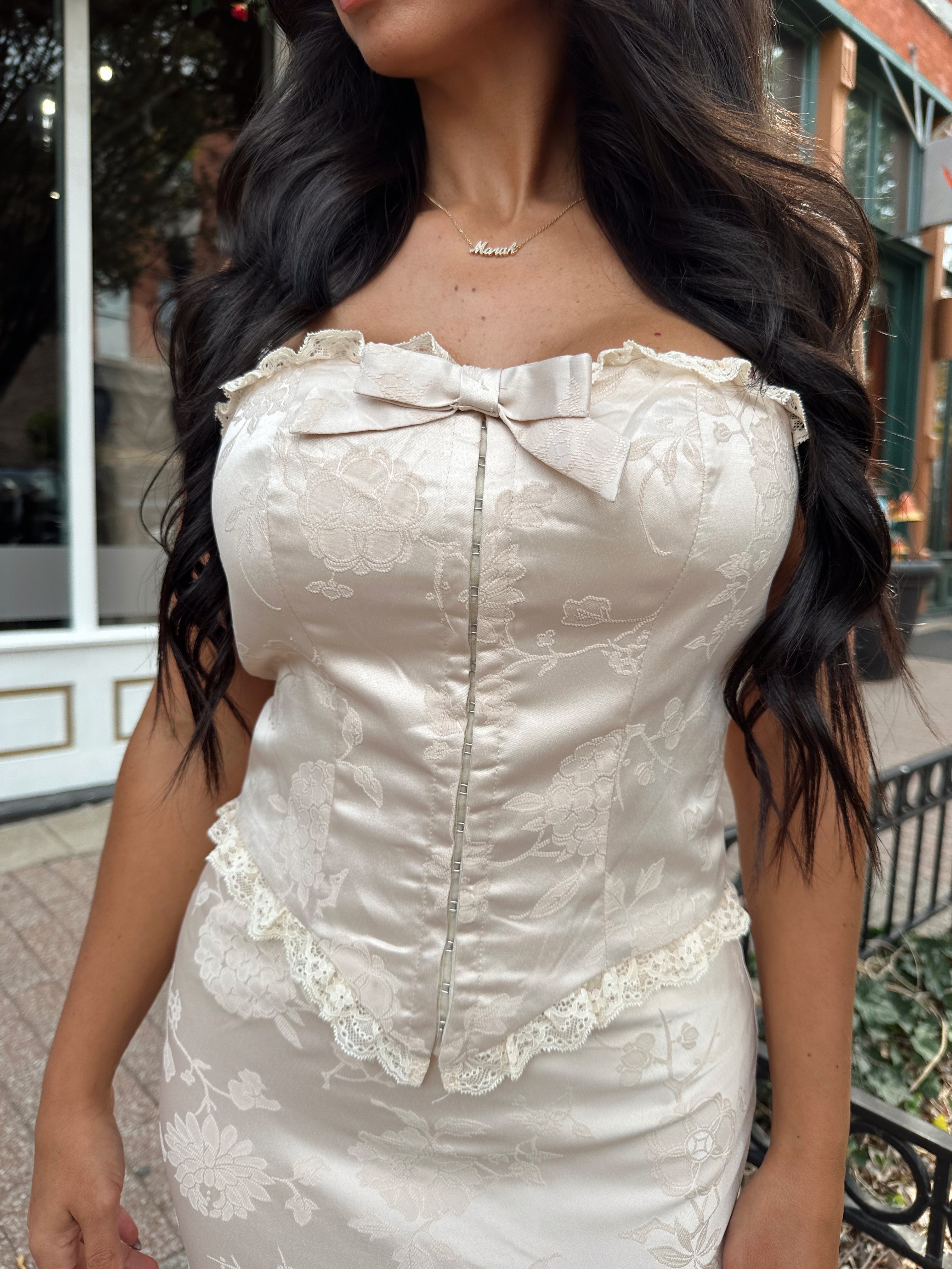 Woman wearing champagne floral satin two piece set with corset top and maxi skirt. 