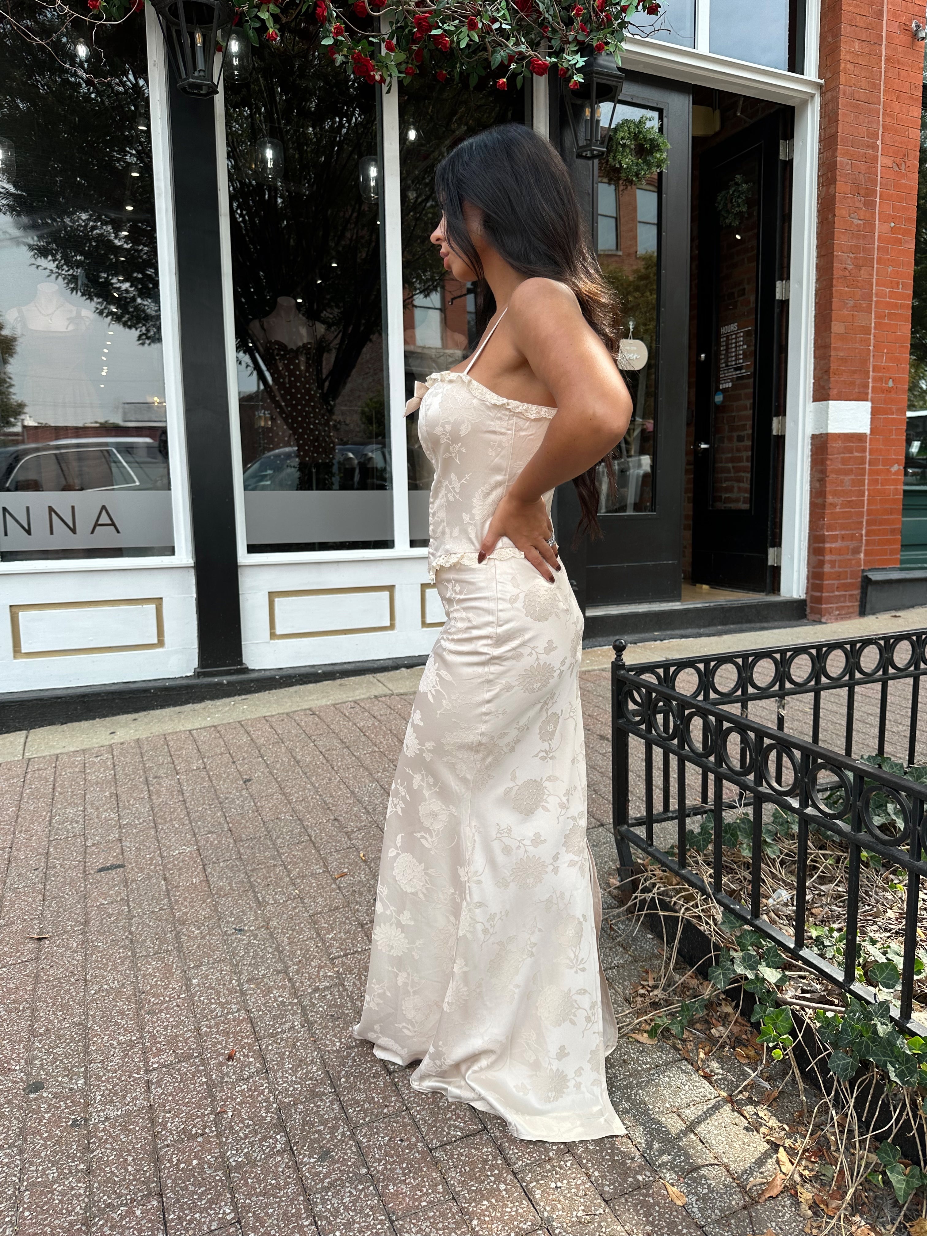 Woman wearing champagne floral satin two piece set with corset top and maxi skirt. 