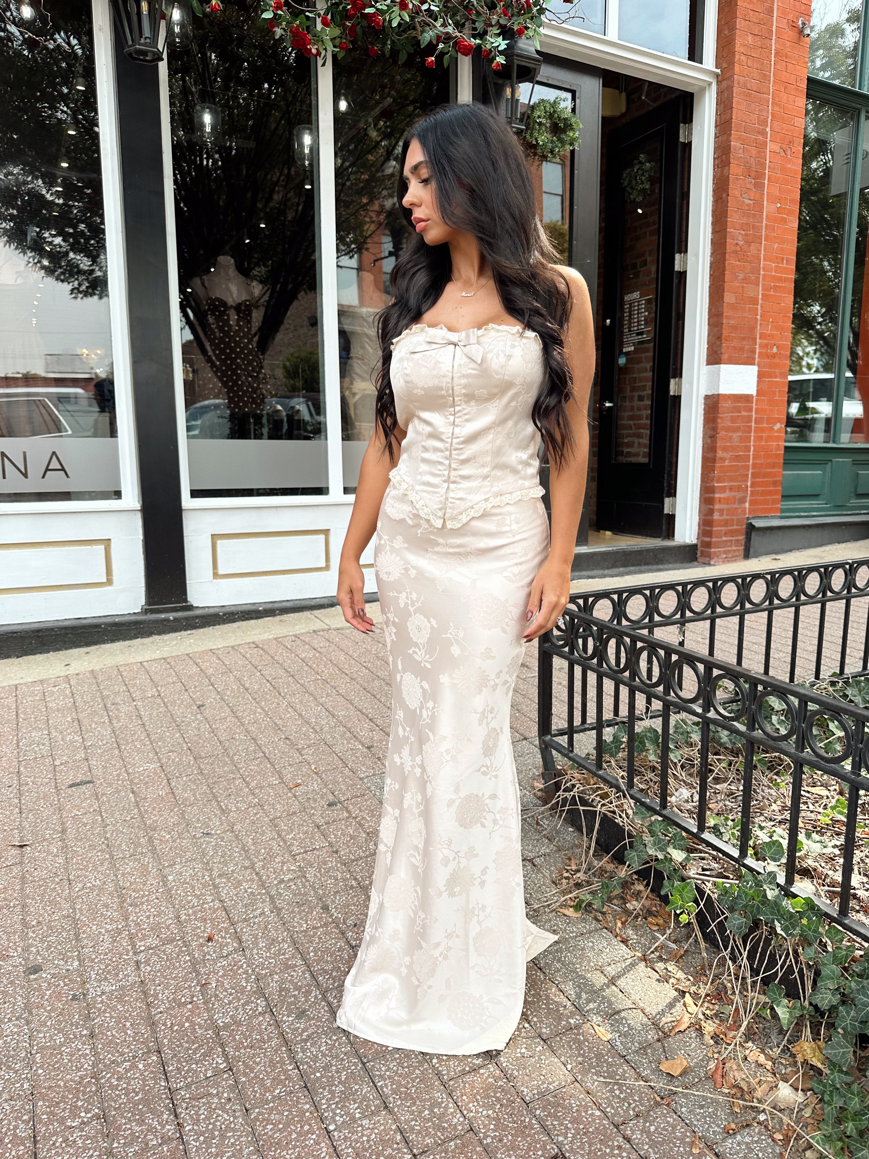 Woman wearing champagne floral satin two piece set with corset top and maxi skirt. 