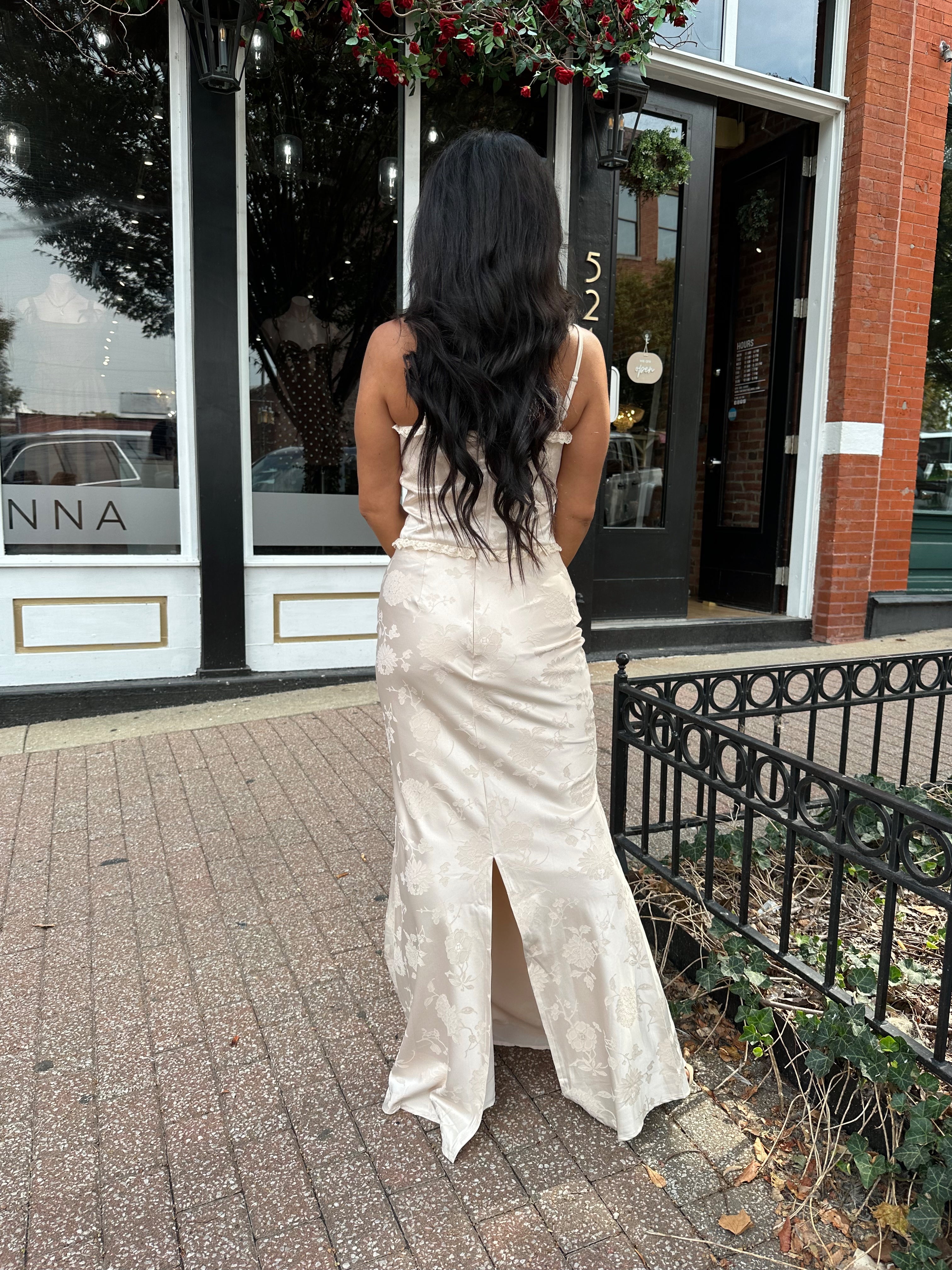 Woman wearing champagne floral satin two piece set with corset top and maxi skirt. 