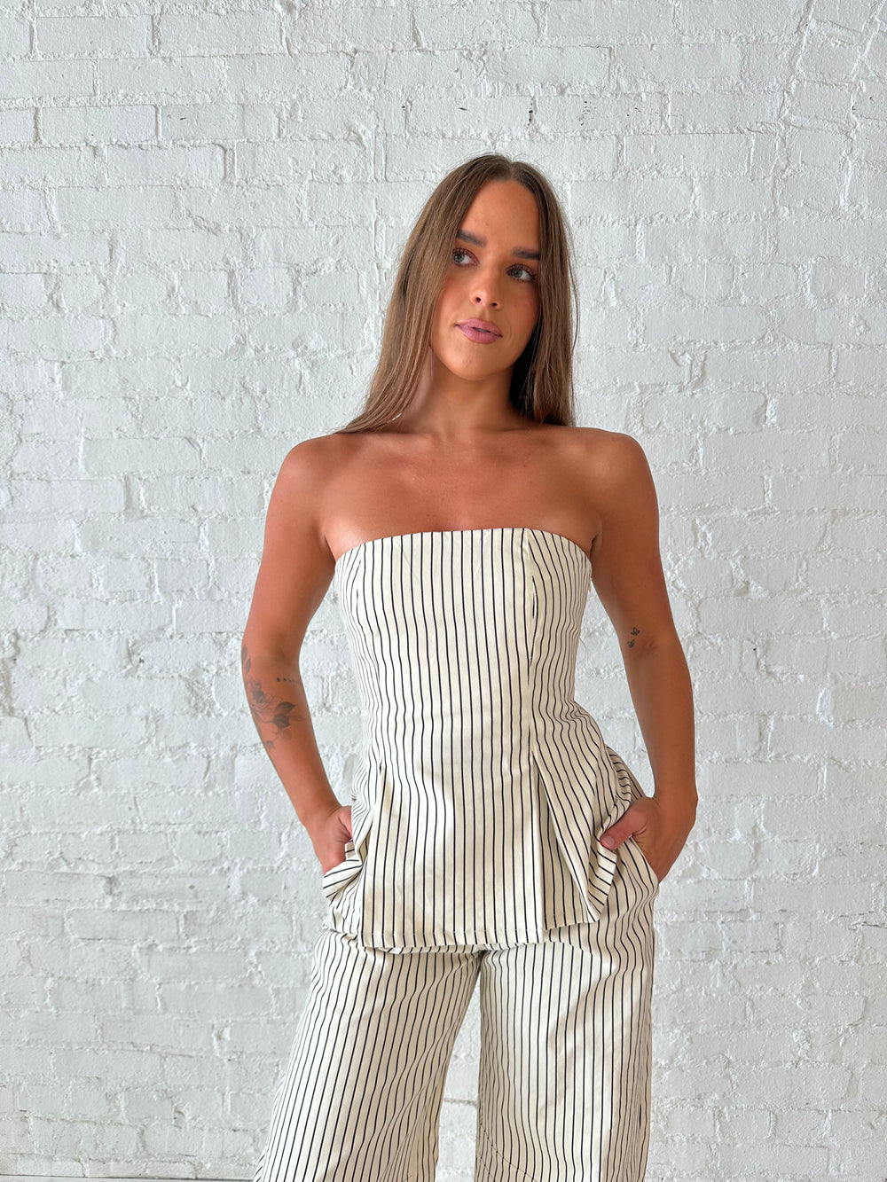 Woman wearing neutral striped two piece set with strapless peplum top, and barrel pant. 