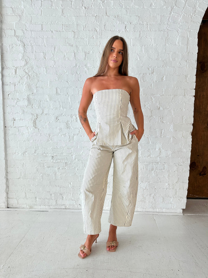 Woman wearing neutral striped two piece set with strapless peplum top, and barrel pant. 