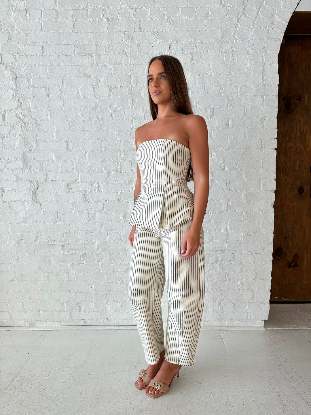 Woman wearing neutral striped two piece set with strapless peplum top, and barrel pant. 