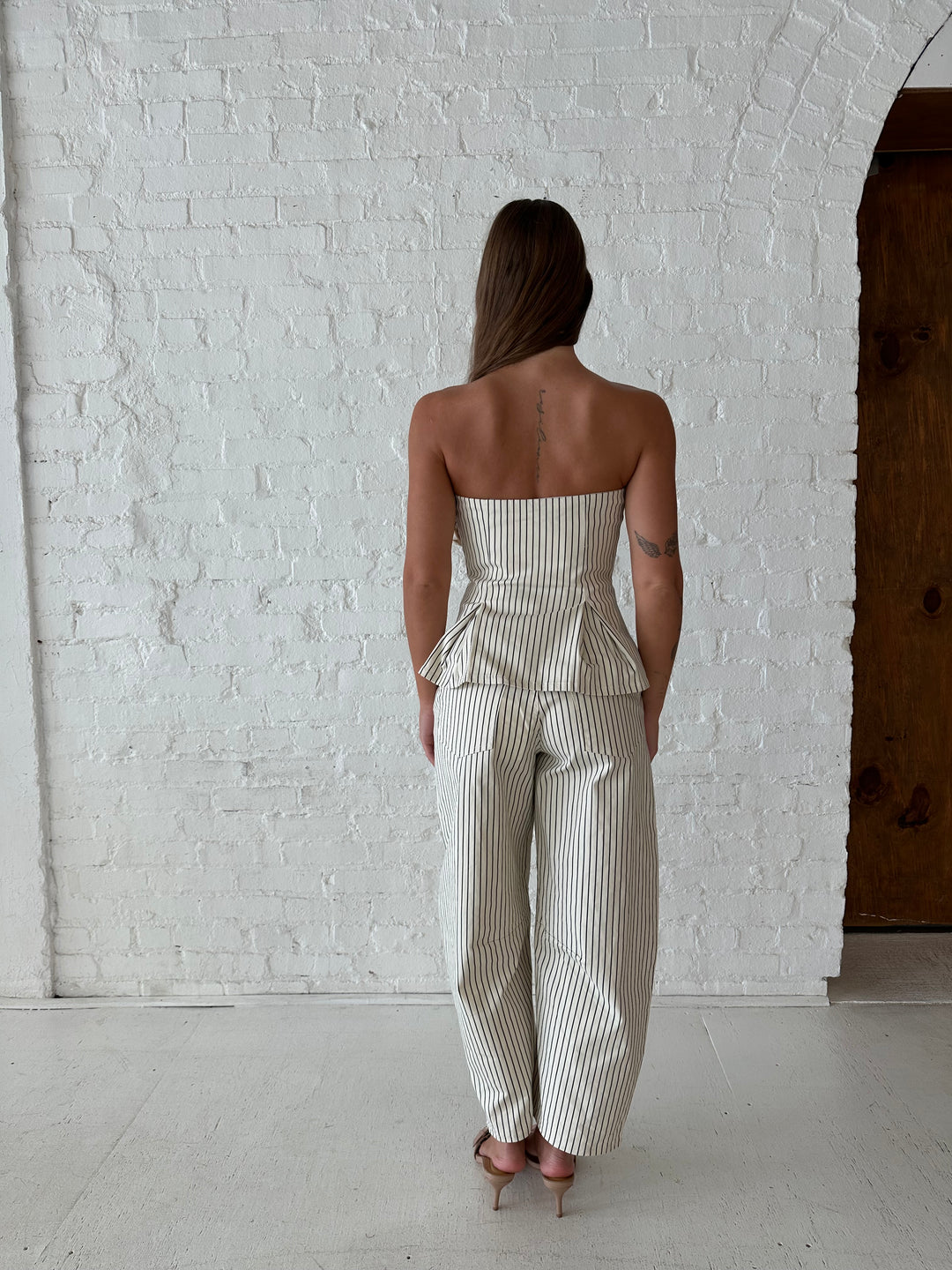 Woman wearing neutral striped two piece set with strapless peplum top, and barrel pant. 
