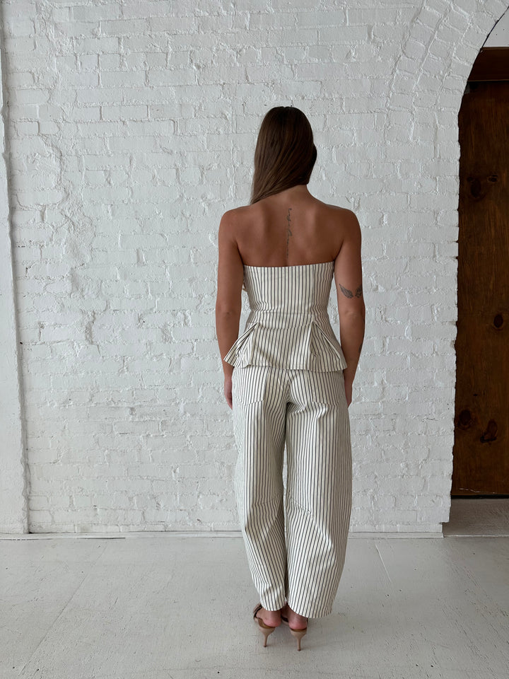 Woman wearing neutral striped two piece set with strapless peplum top, and barrel pant. 
