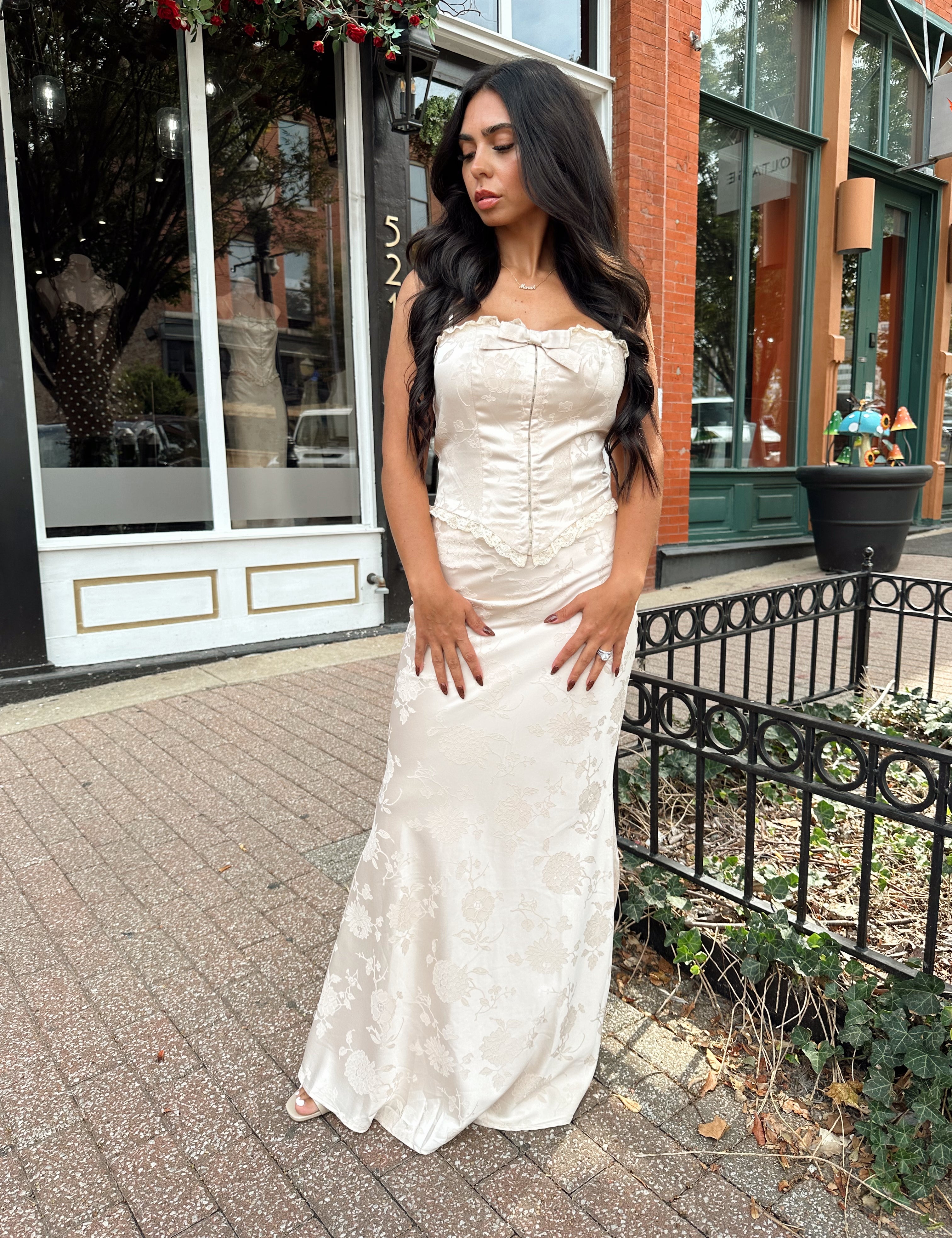 Woman wearing champagne floral satin two piece set with corset top and maxi skirt. 