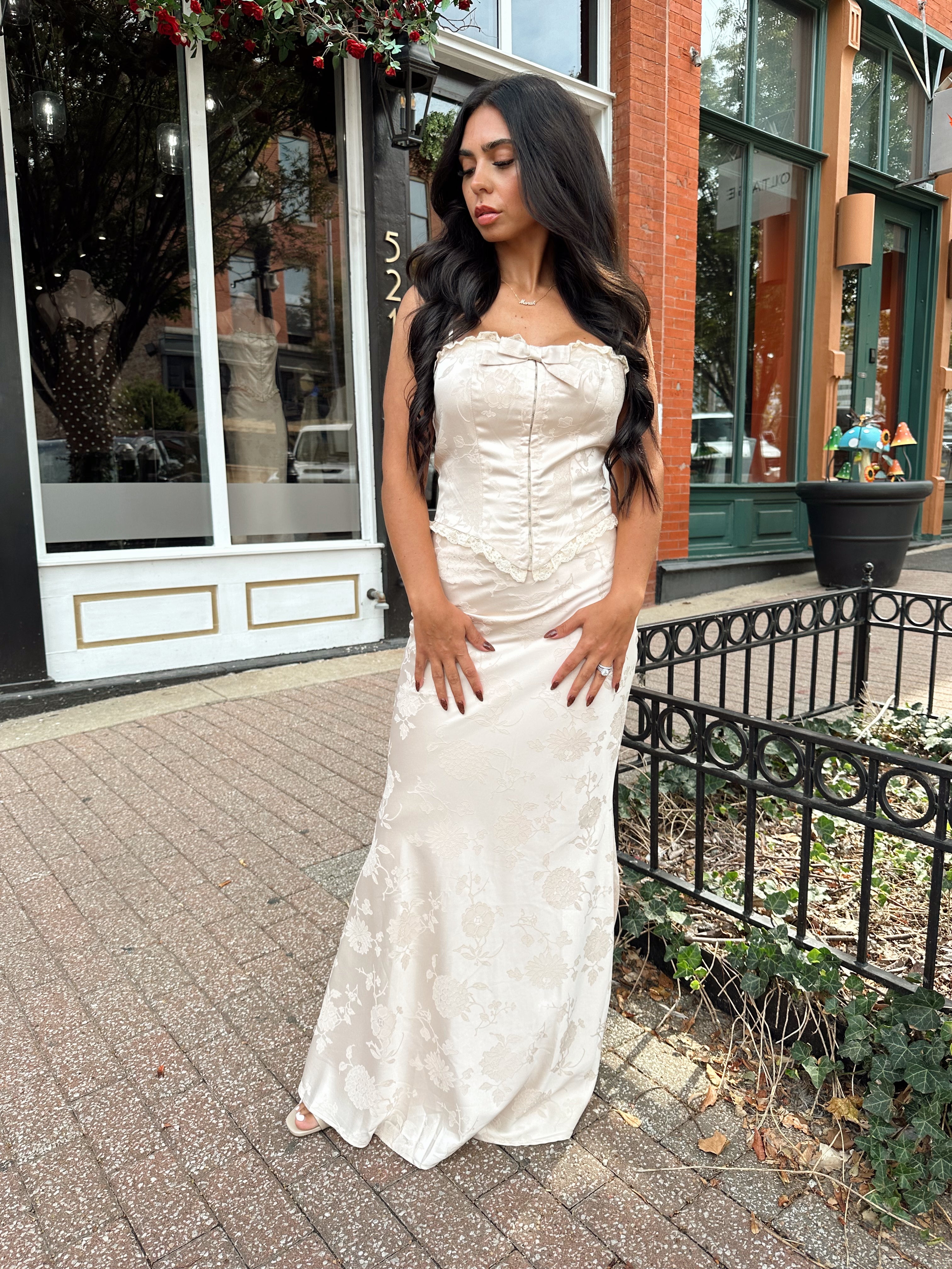 Woman wearing champagne floral satin two piece set with corset top and maxi skirt. 