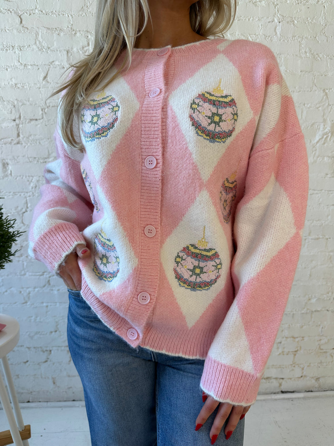 Woman wearing pink and white button down cardigan with embroidered ornaments. 