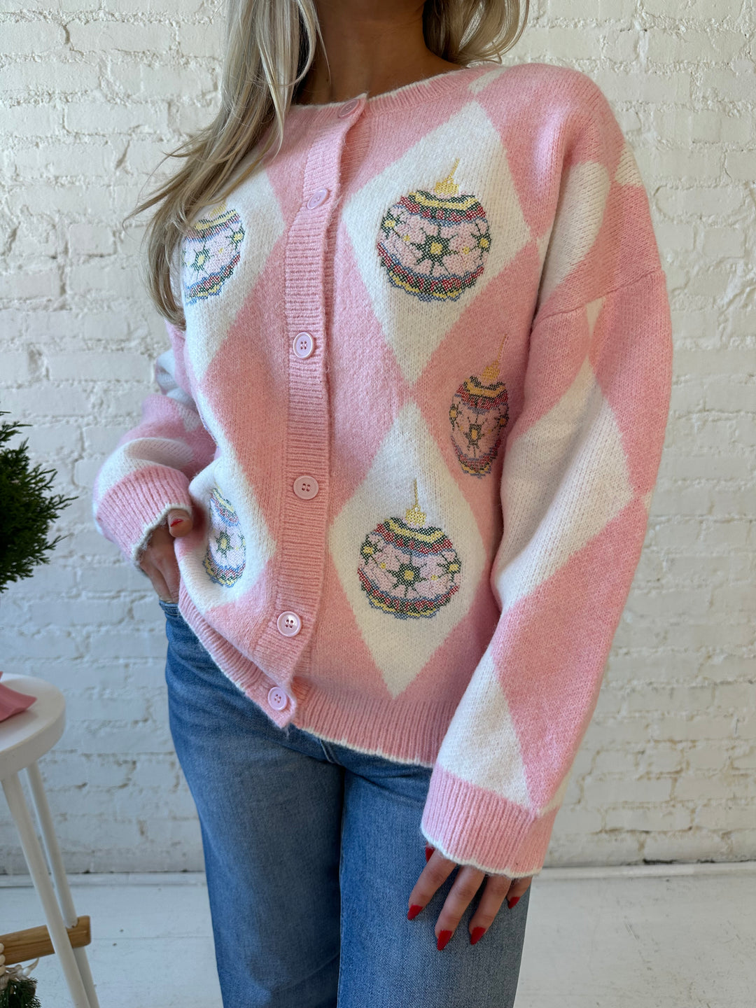 Woman wearing pink and white button down cardigan with embroidered ornaments. 