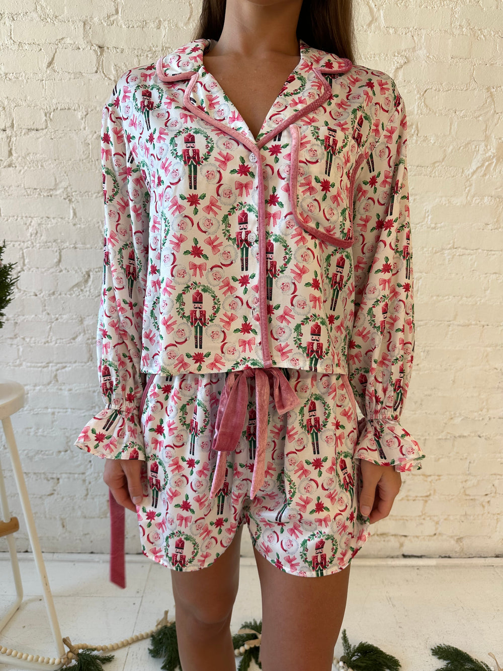 Woman wearing pink nutcracker satin pajama set with green wreath detailing and pink velvet trim. 