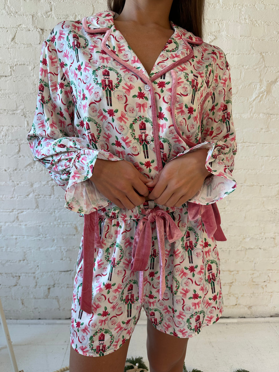 Woman wearing pink nutcracker satin pajama set with green wreath detailing and pink velvet trim. 