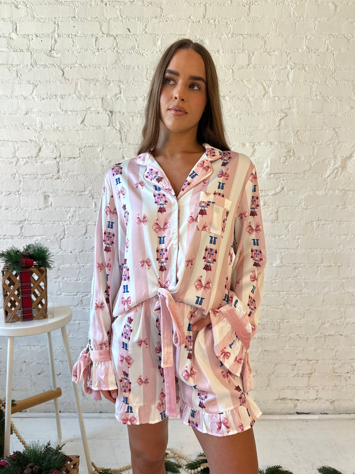 Woman wearing pink and white striped satin pajamas with pink nutcrackers all over.