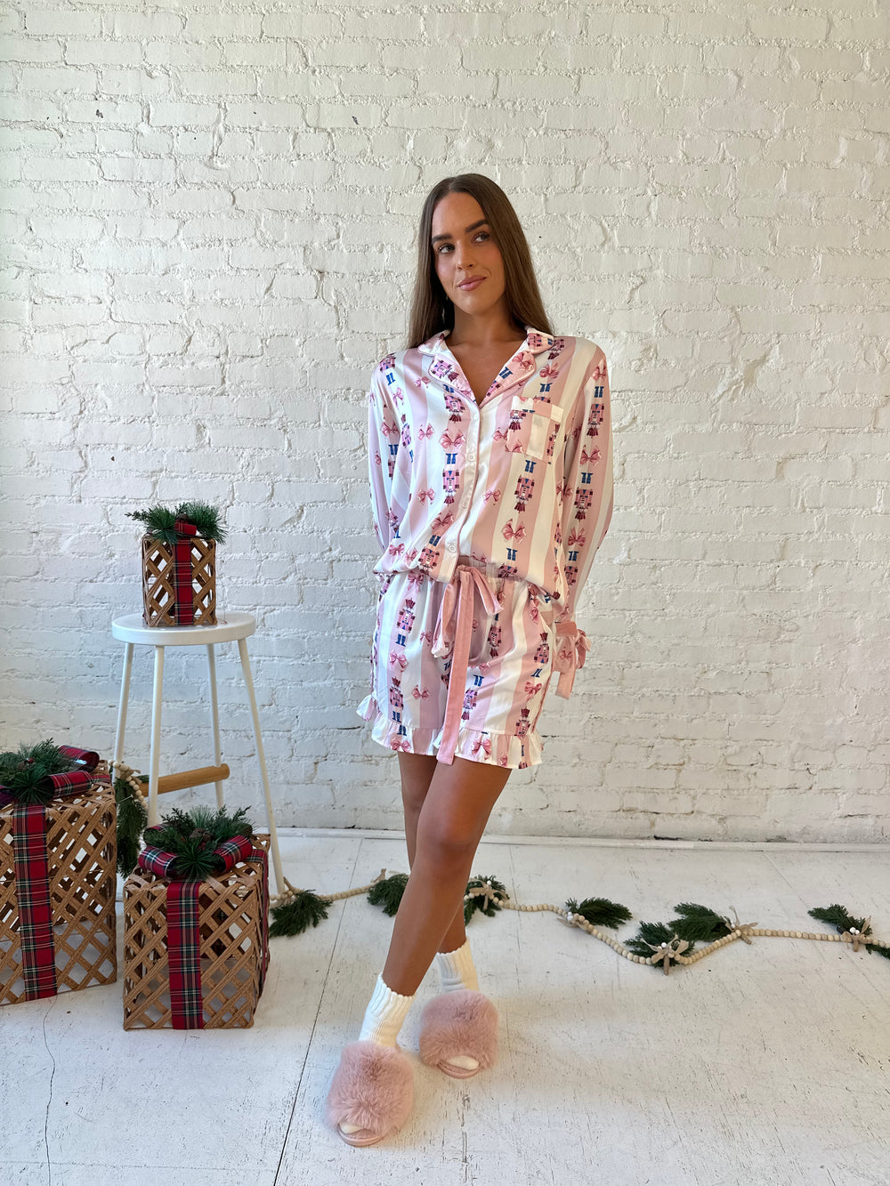 Woman wearing pink and white striped satin pajamas with pink nutcrackers all over.