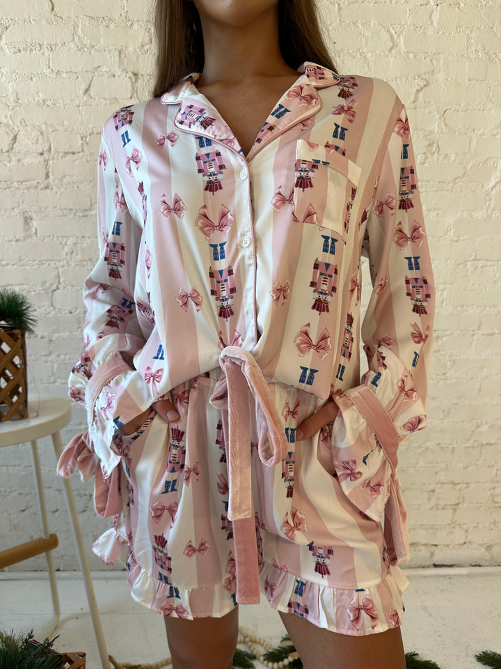 Woman wearing pink and white striped satin pajamas with pink nutcrackers all over.