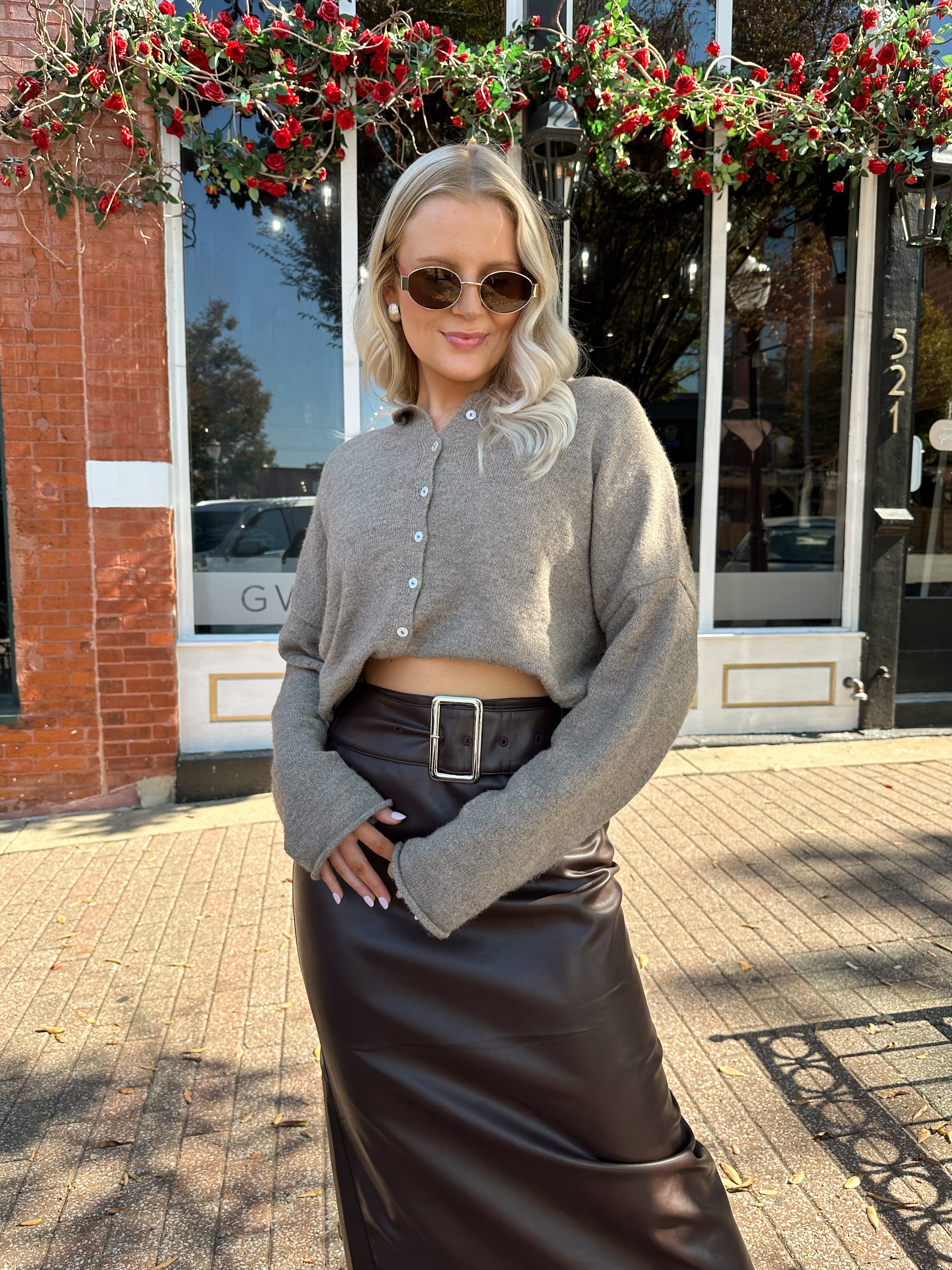 Woman wearing mocha knit button down cardigan with brown leather belted midi skirt.