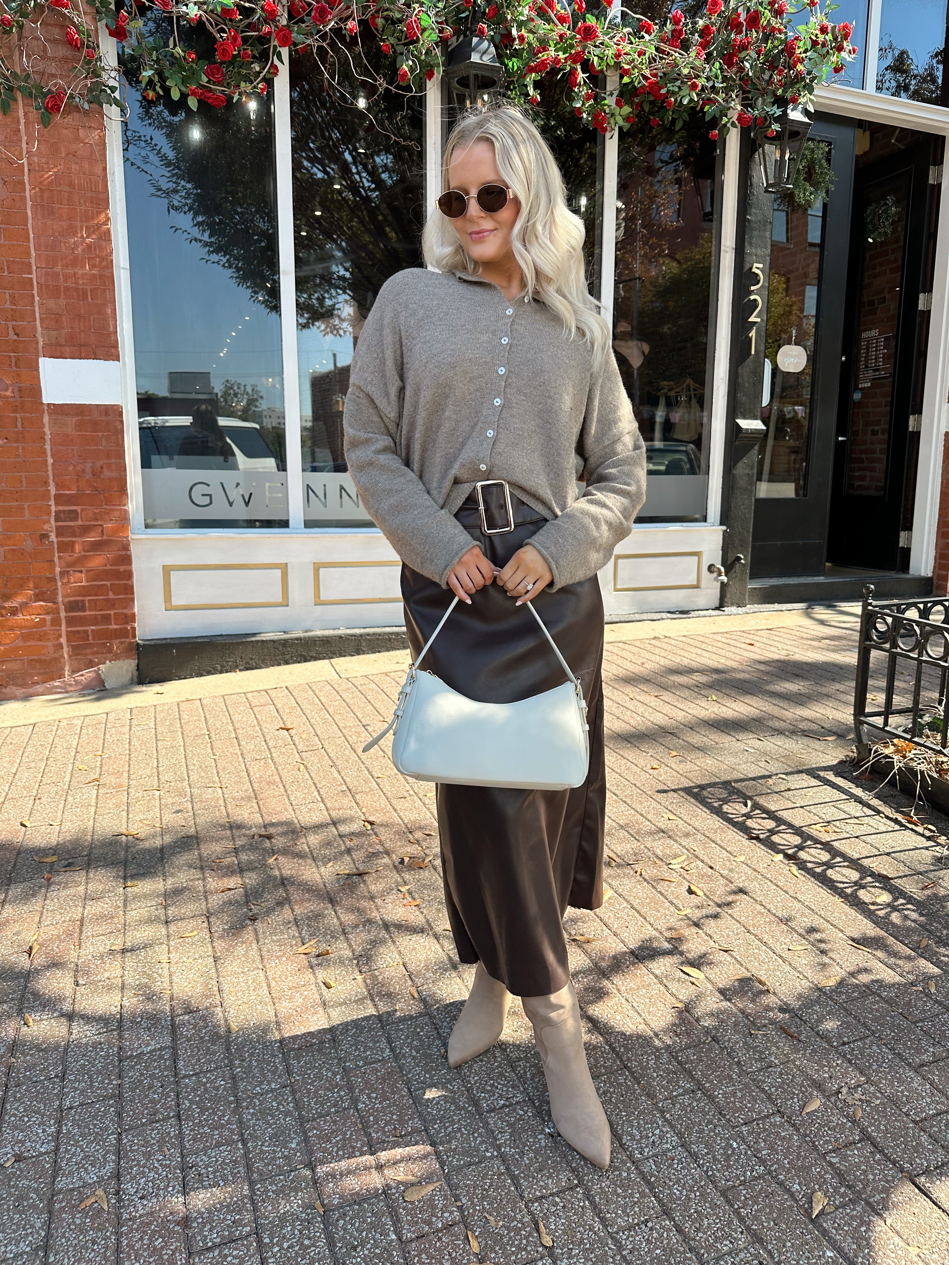 Woman wearing mocha knit button down cardigan with brown leather belted midi skirt.