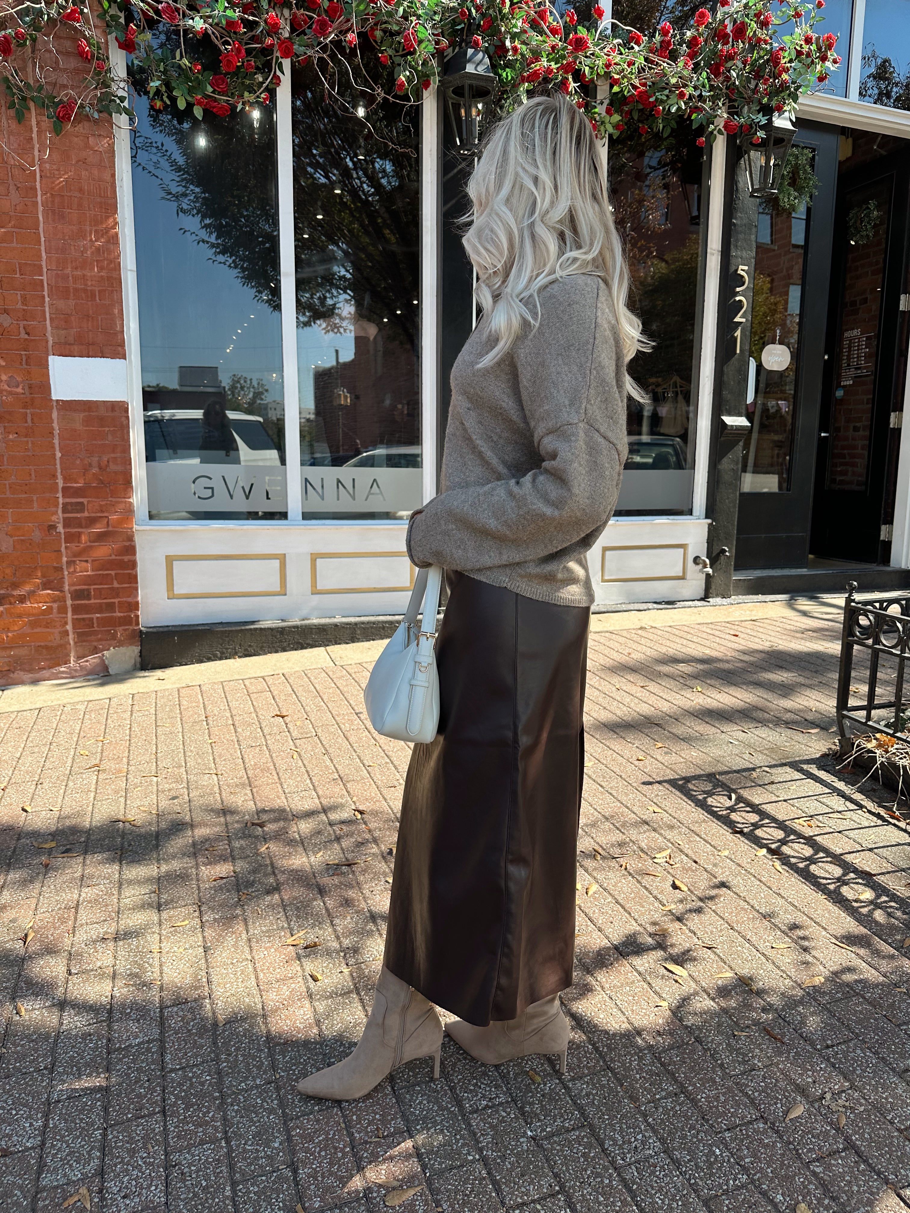 Woman wearing mocha knit button down cardigan with brown leather belted midi skirt.