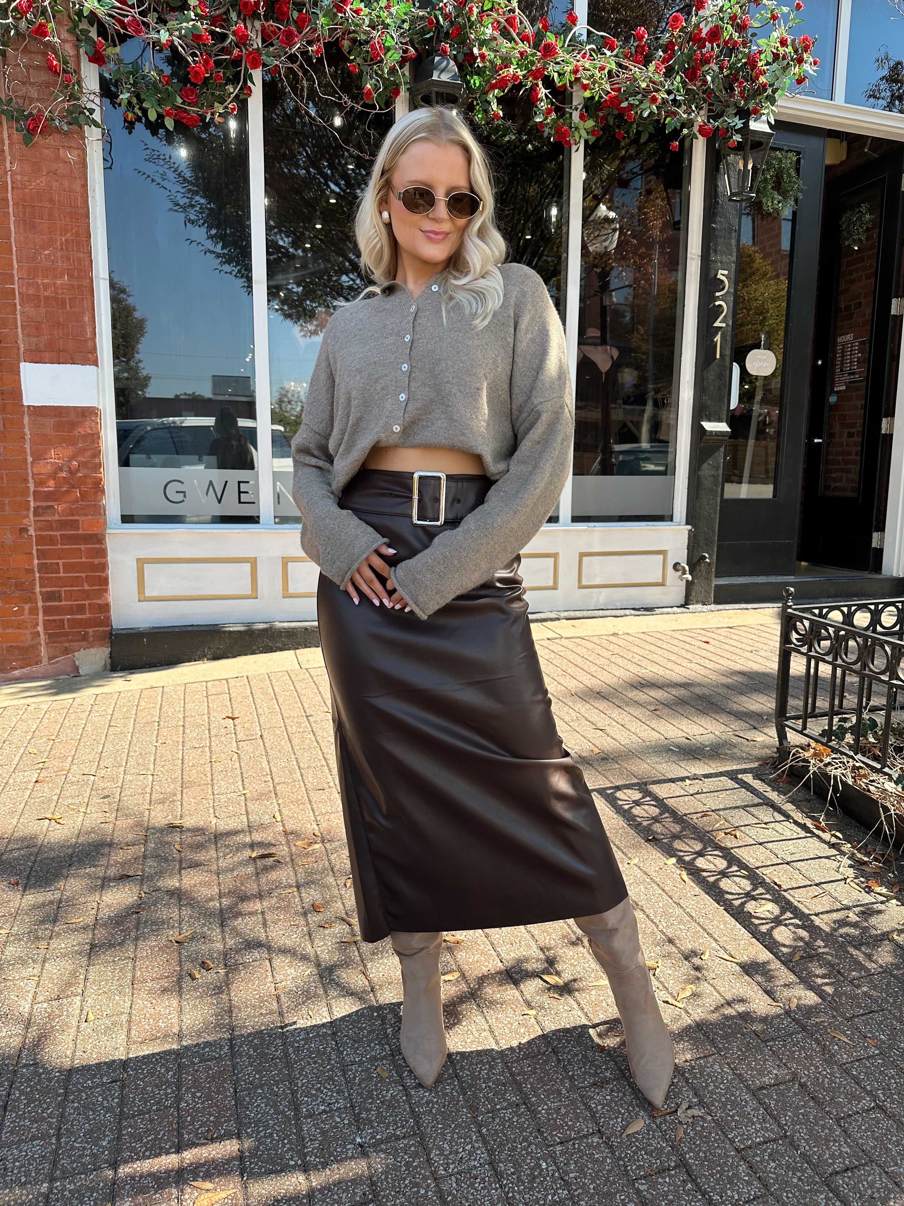 Woman wearing mocha knit button down cardigan with brown leather belted midi skirt.