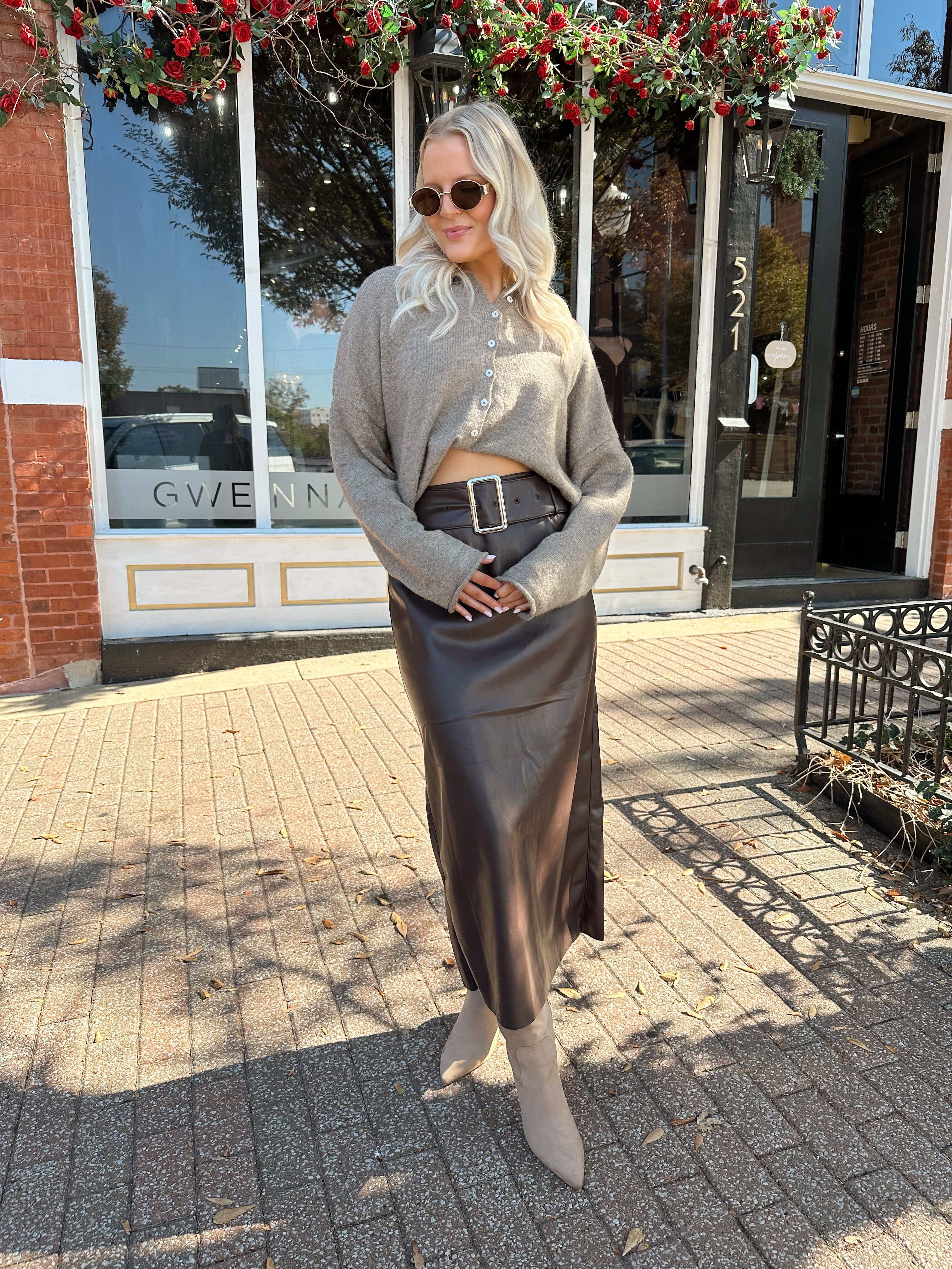 Woman wearing mocha knit button down cardigan with brown leather belted midi skirt.