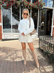 Woman wearing white knit button down cardigan with pleated mini skirt. 