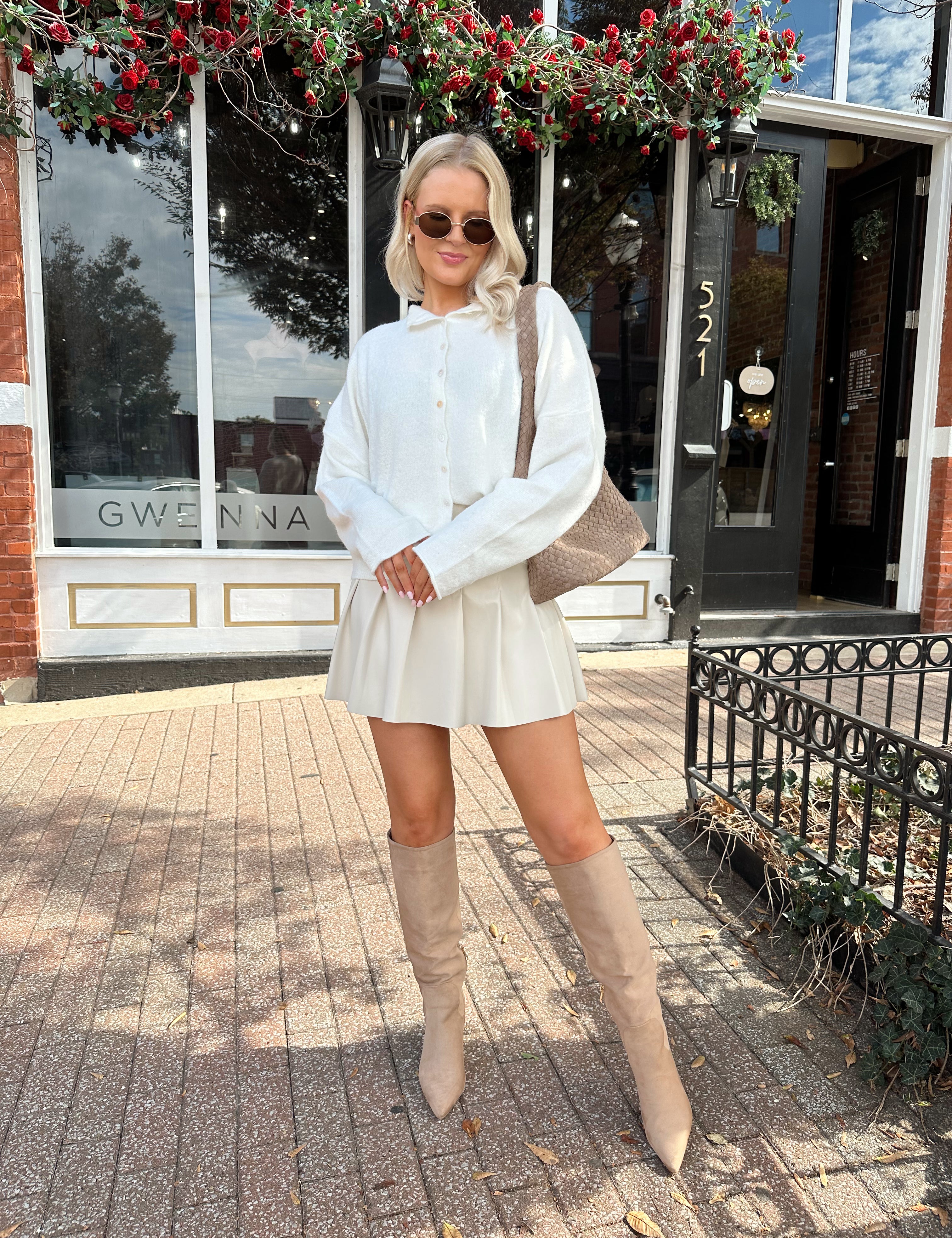 Woman wearing white knit button down cardigan with pleated mini skirt. 