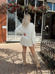 Woman wearing white knit button down cardigan with pleated mini skirt. 