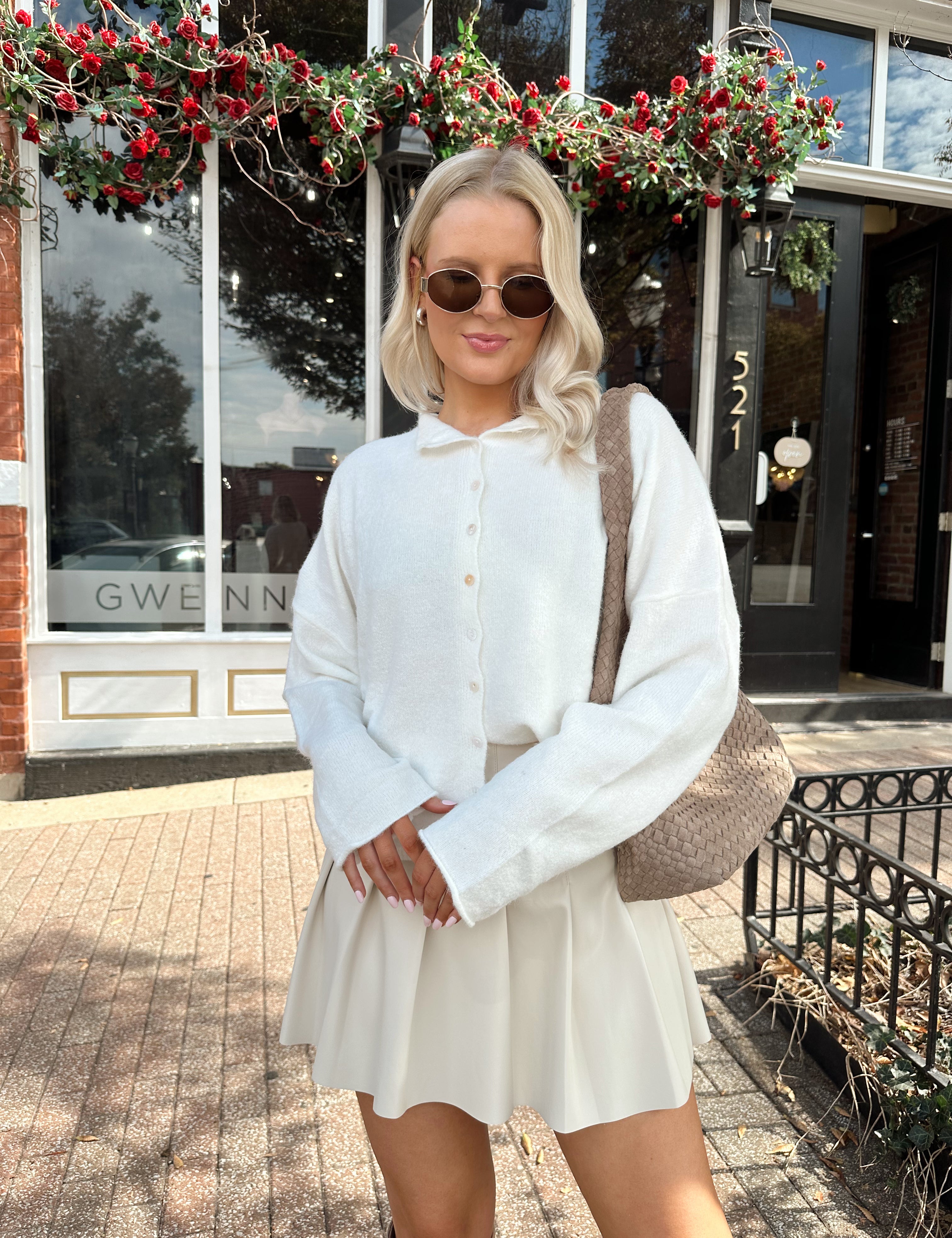 Woman wearing white knit button down cardigan with pleated mini skirt. 