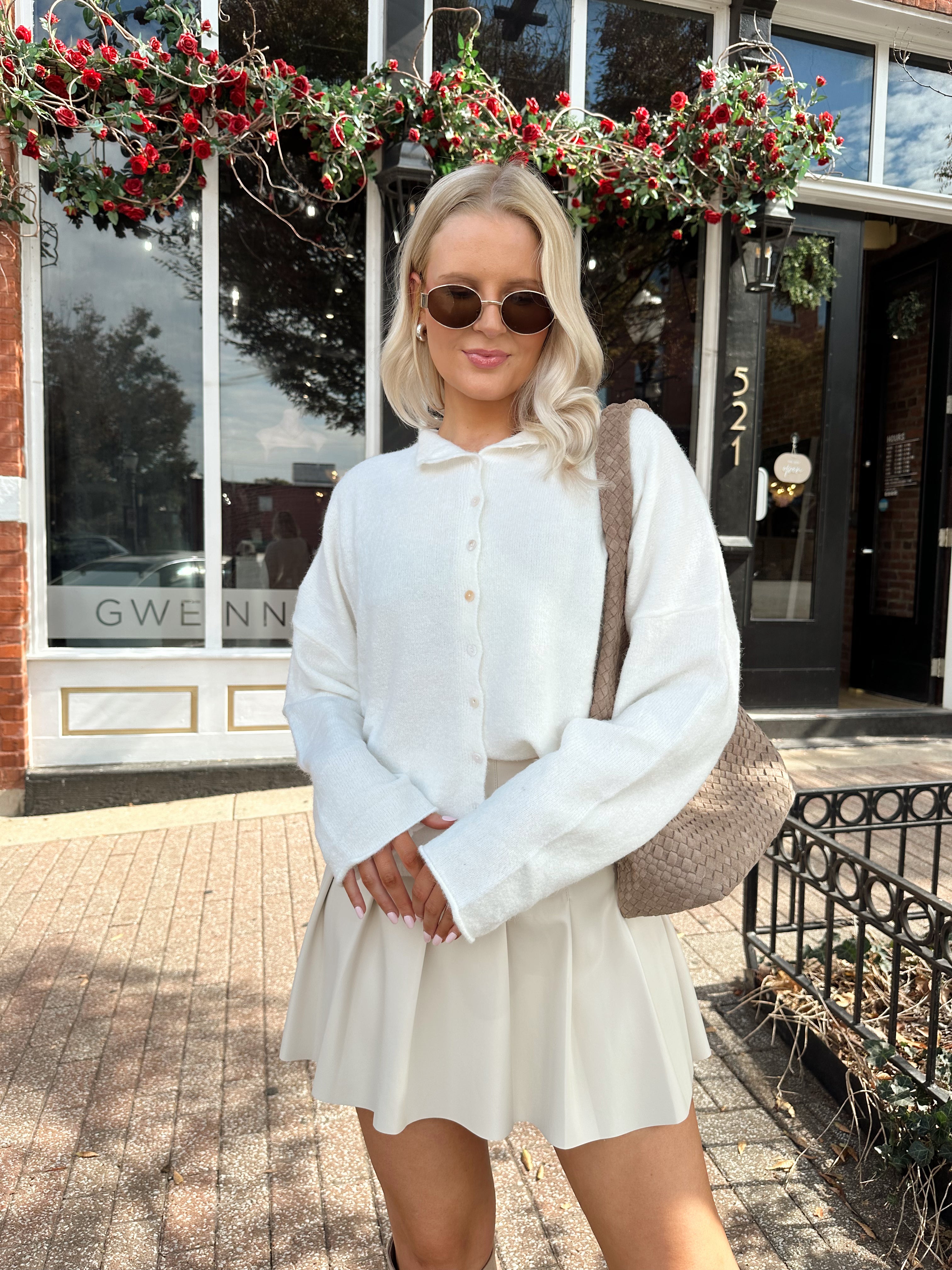 Woman wearing white knit button down cardigan with pleated mini skirt. 