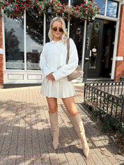 Woman wearing white knit button down cardigan with pleated mini skirt. 