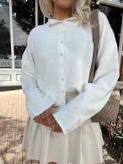 Woman wearing white knit button down cardigan with pleated mini skirt. 