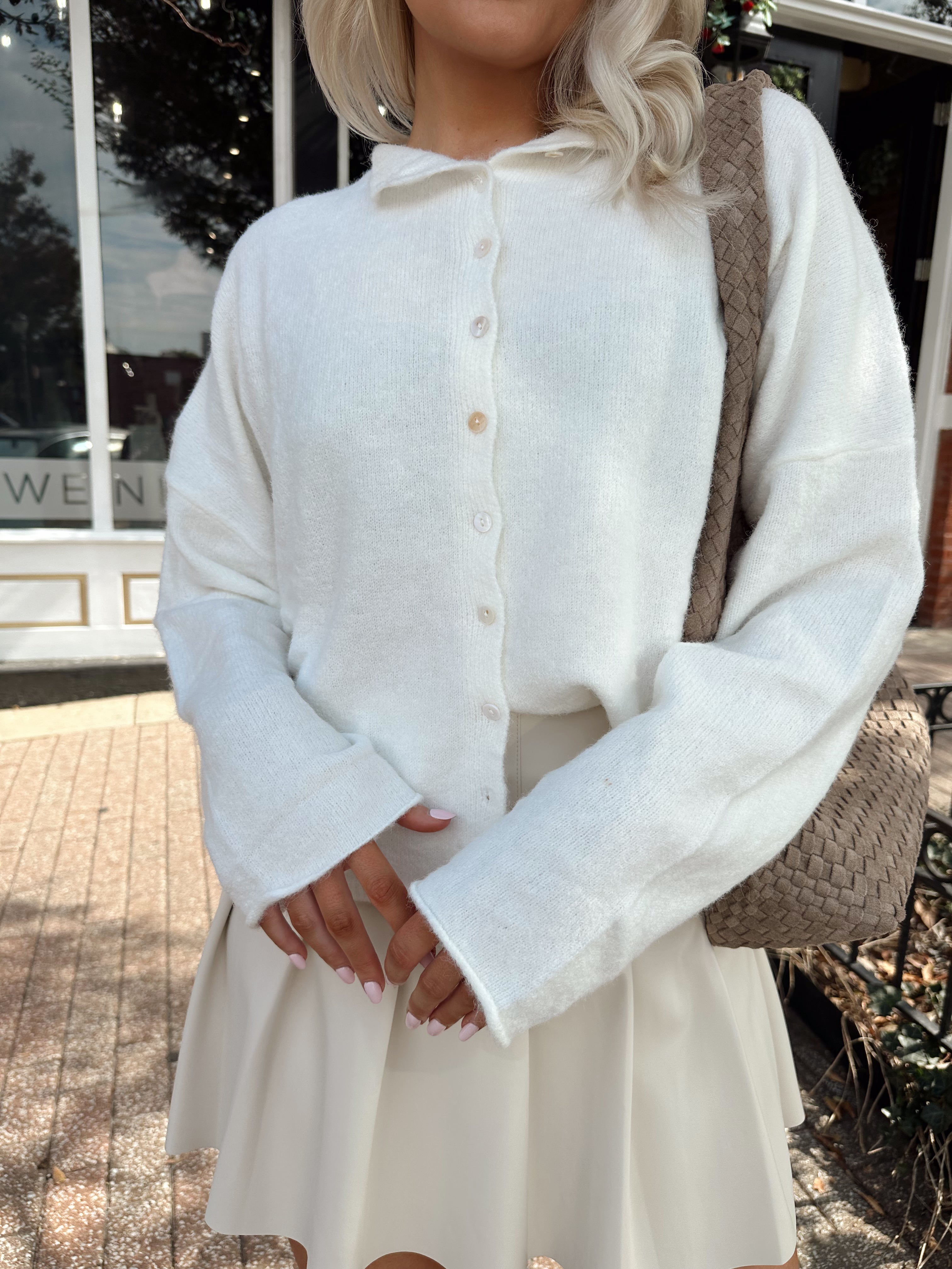 Woman wearing white knit button down cardigan with pleated mini skirt. 