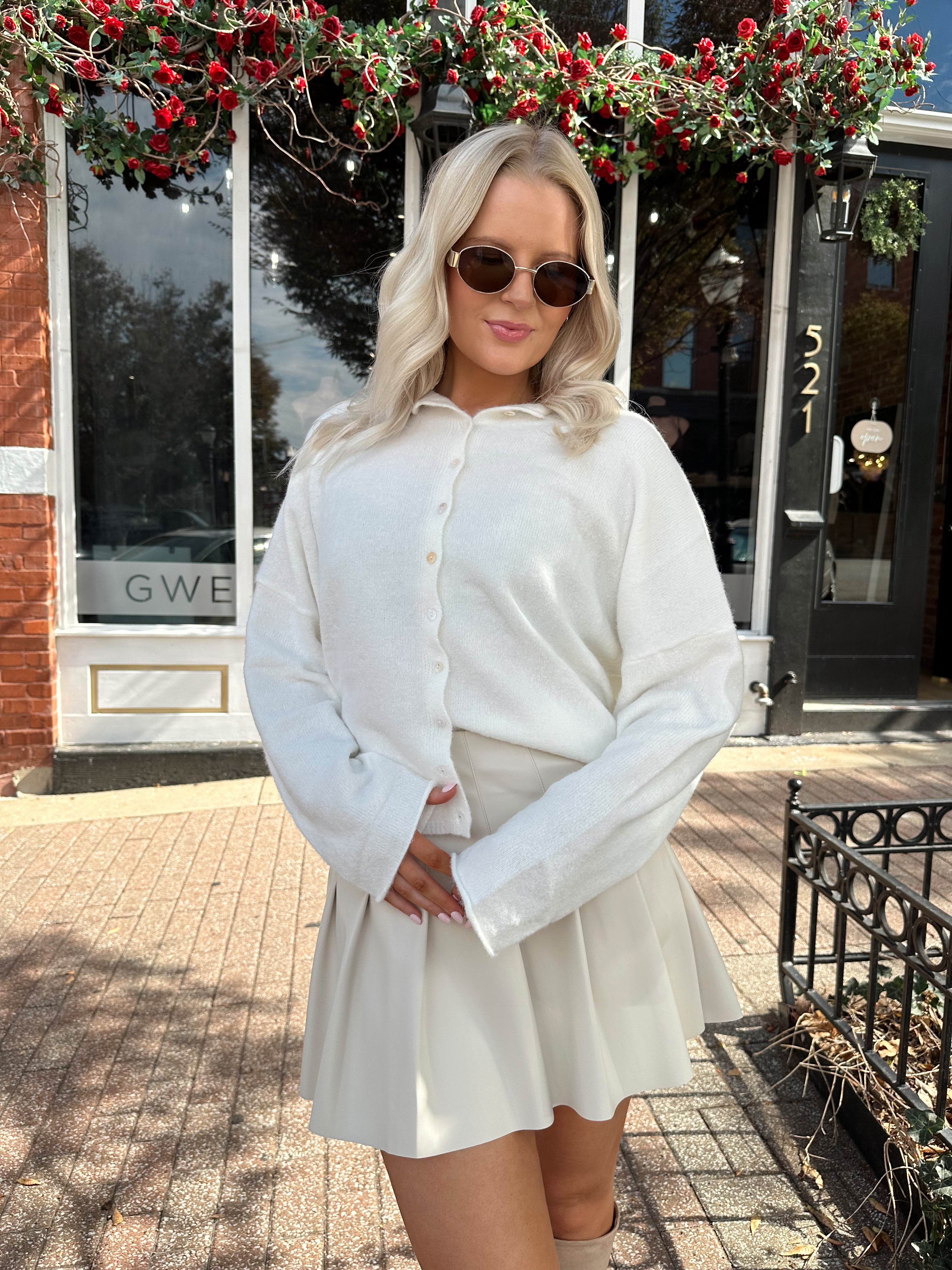 Woman wearing white knit button down cardigan with pleated mini skirt. 