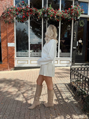 Woman wearing white knit button down cardigan with pleated mini skirt. 