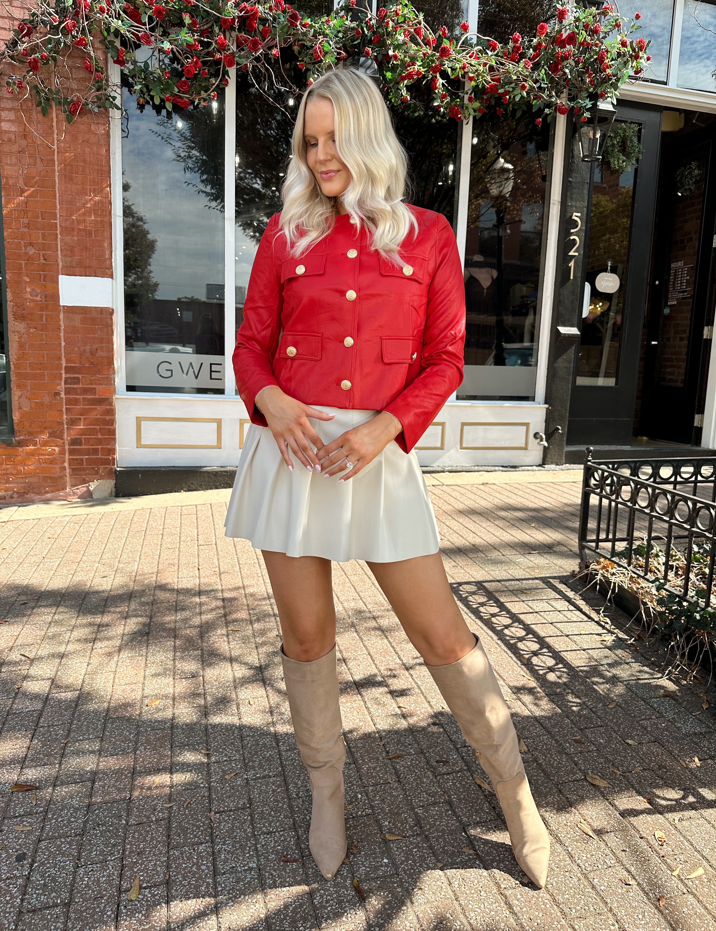 Woman wearing red faux leather jacket with gold button closure. 