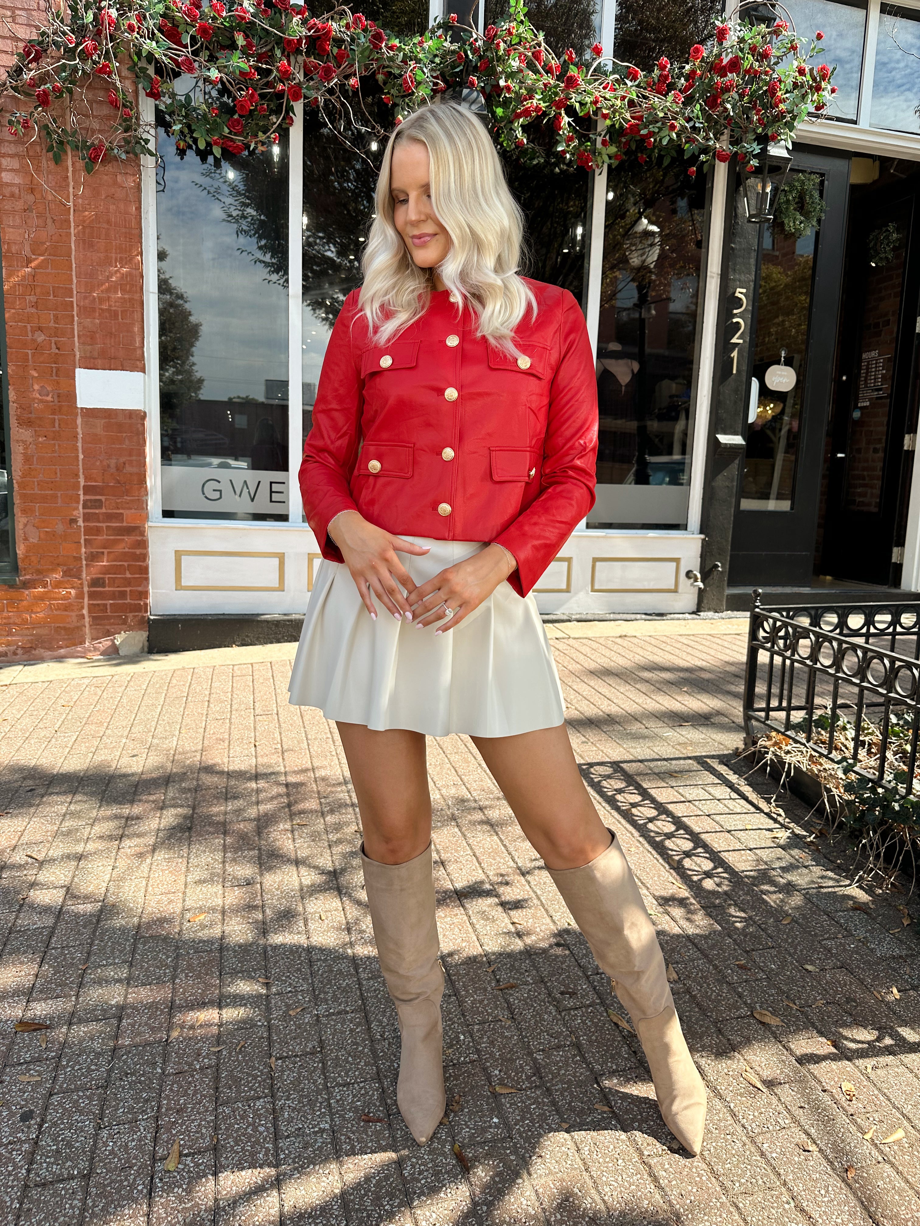 Woman wearing red faux leather jacket with gold button closure. 