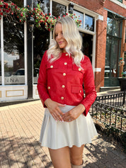 Woman wearing red faux leather jacket with gold button closure. 