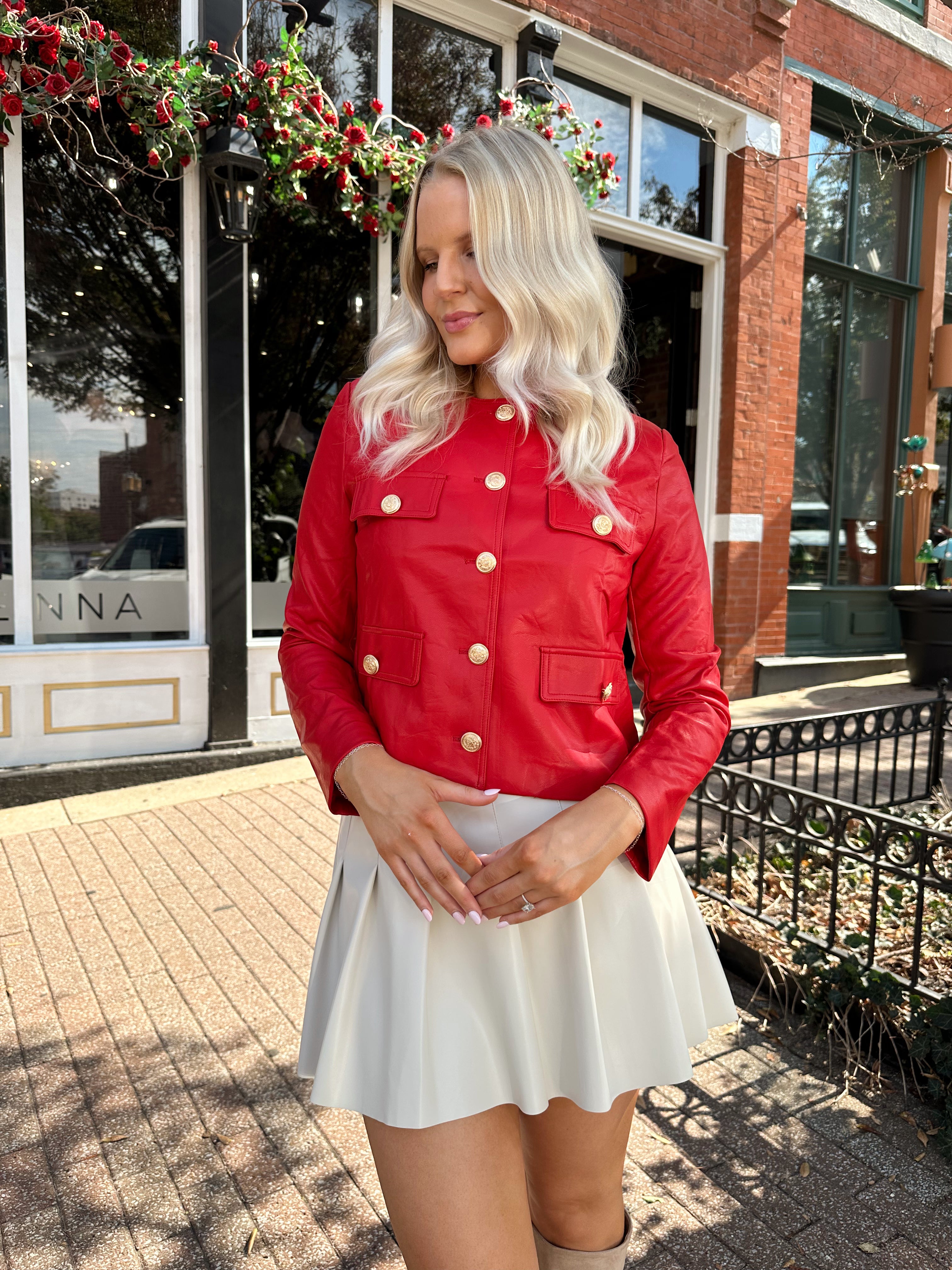 Woman wearing red faux leather jacket with gold button closure. 