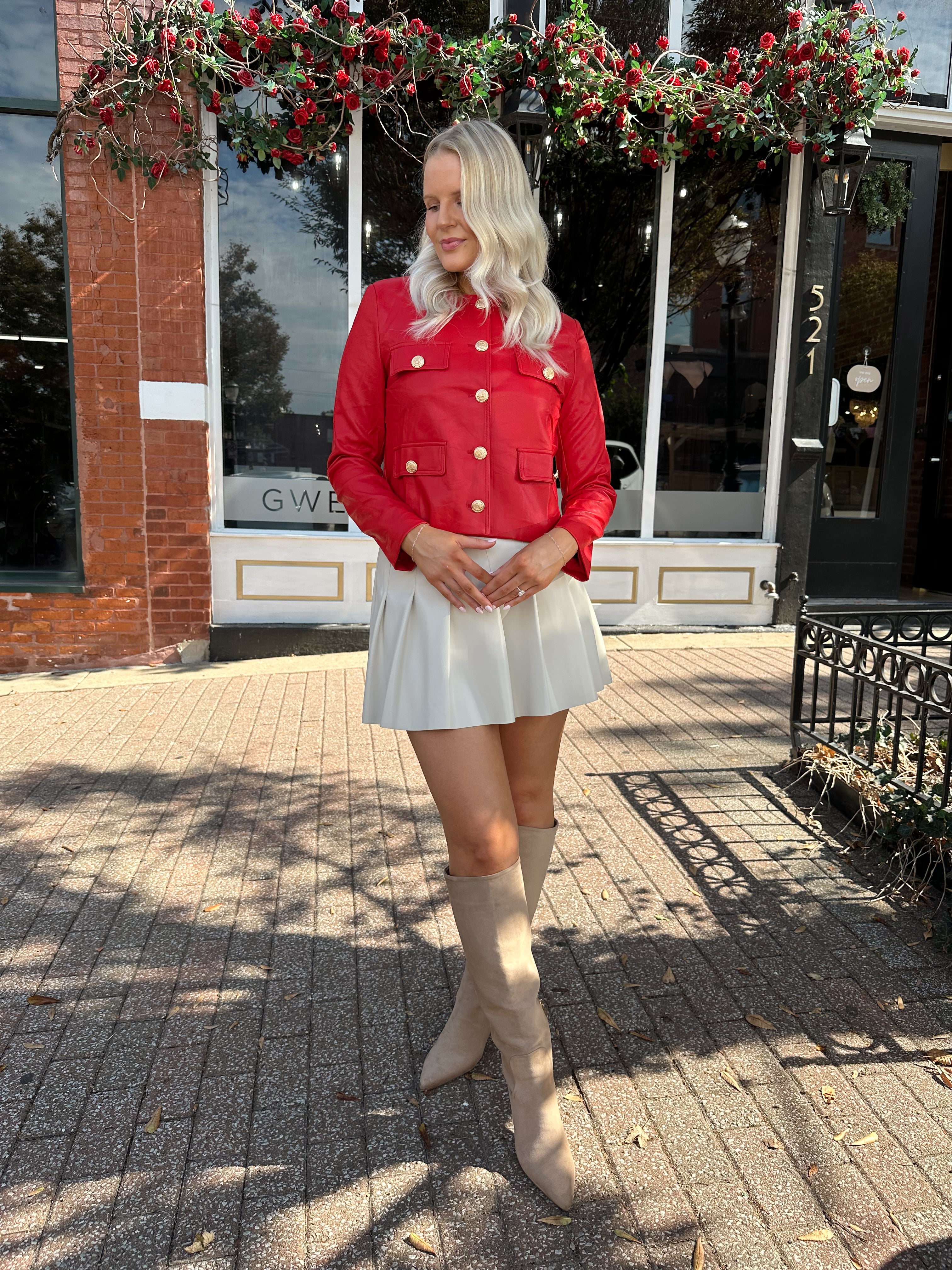 Woman wearing red faux leather jacket with gold button closure. 