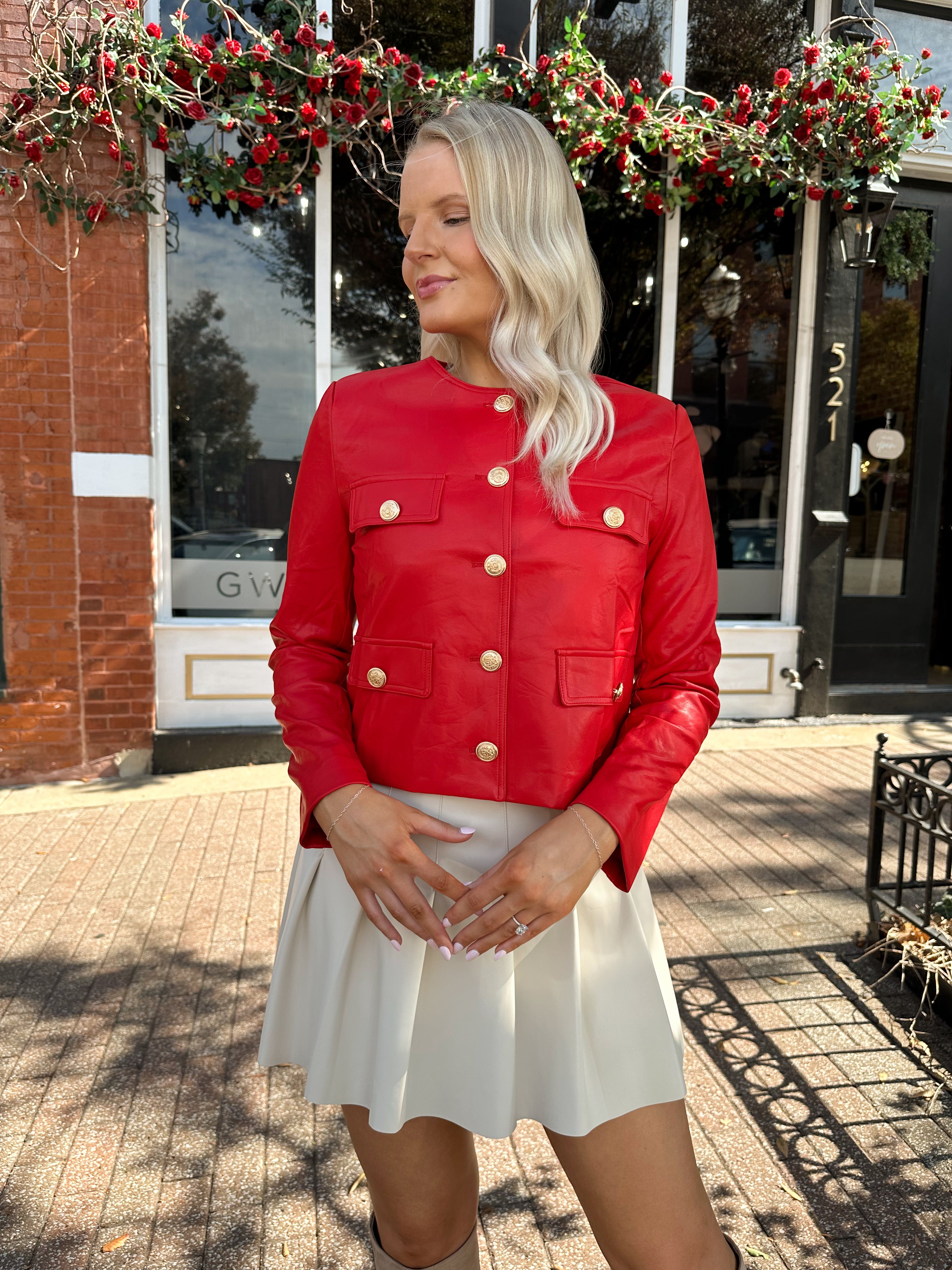 Woman wearing red faux leather jacket with gold button closure. 