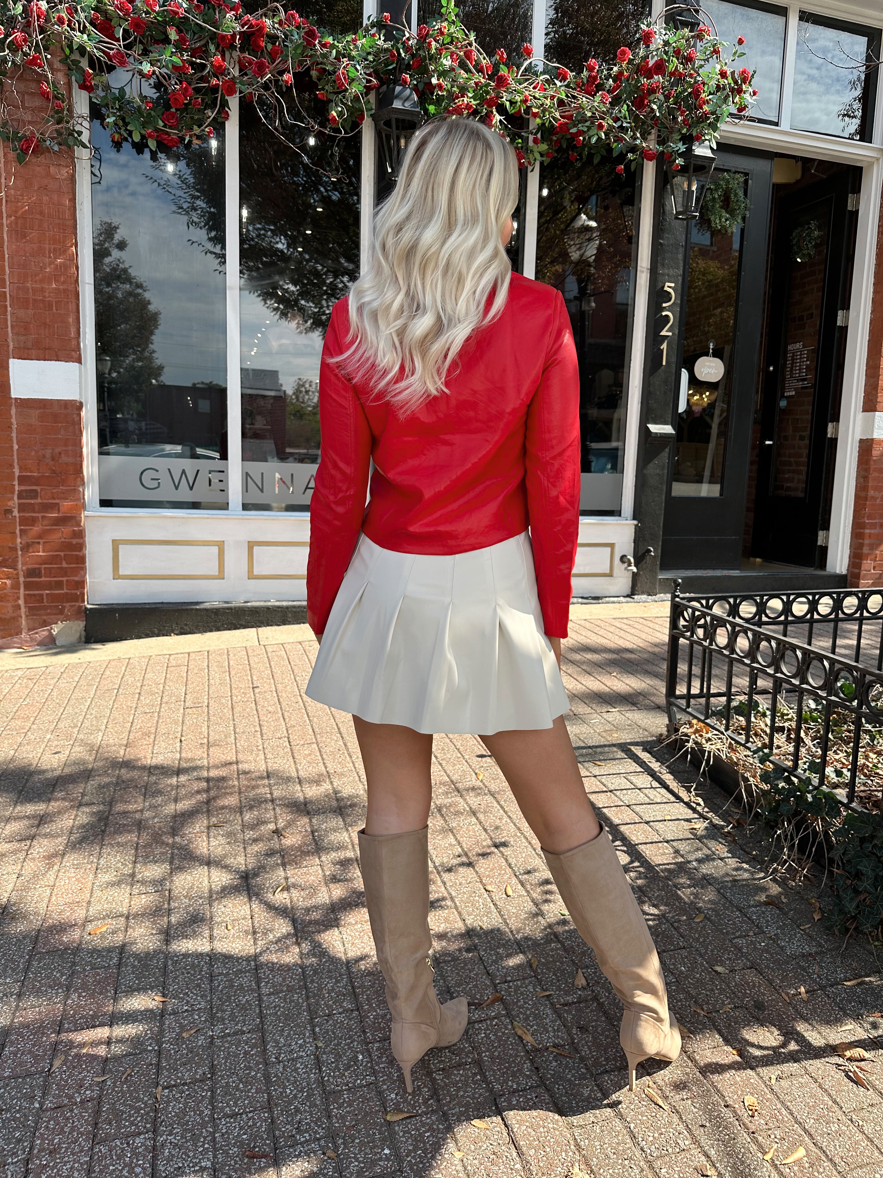 Woman wearing red faux leather jacket with gold button closure. 