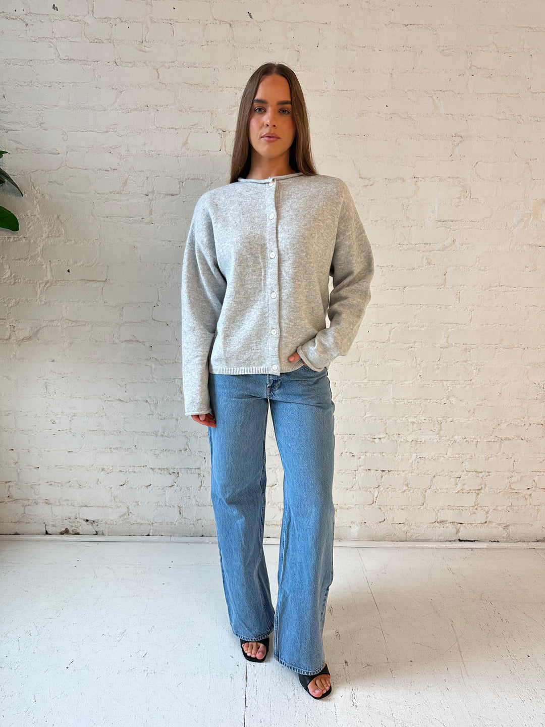 Woman wearing light grey knit button down cardigan with medium wash jeans. 