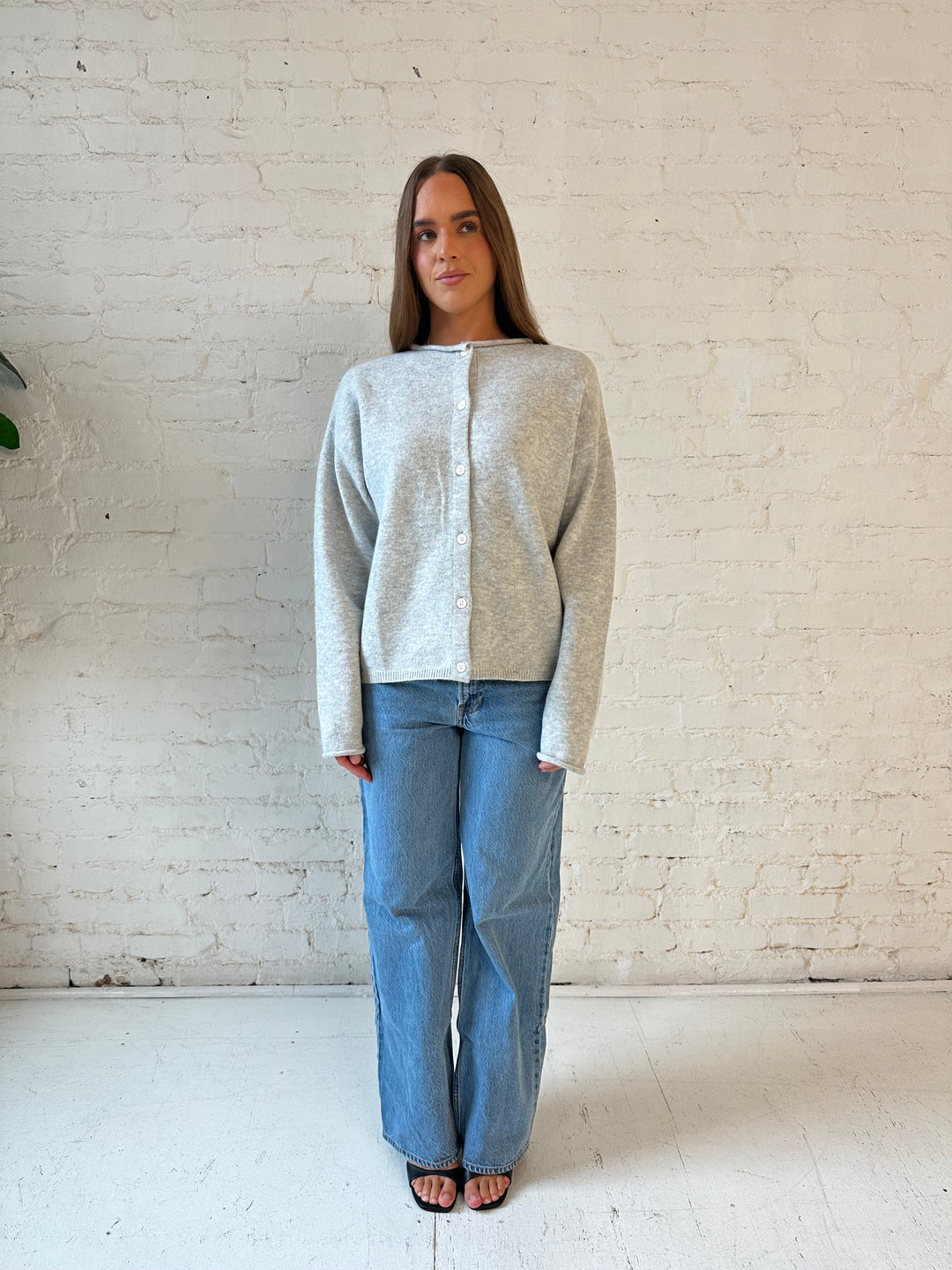 Woman wearing light grey knit button down cardigan with medium wash jeans. 