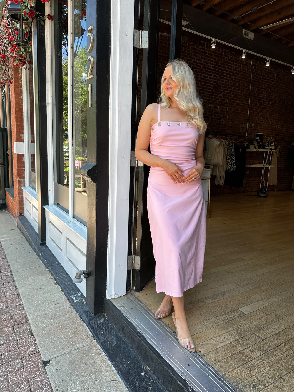 Woman wearing light pink midi dress with ruched sides, adjustable straps, and shell button detailing. 