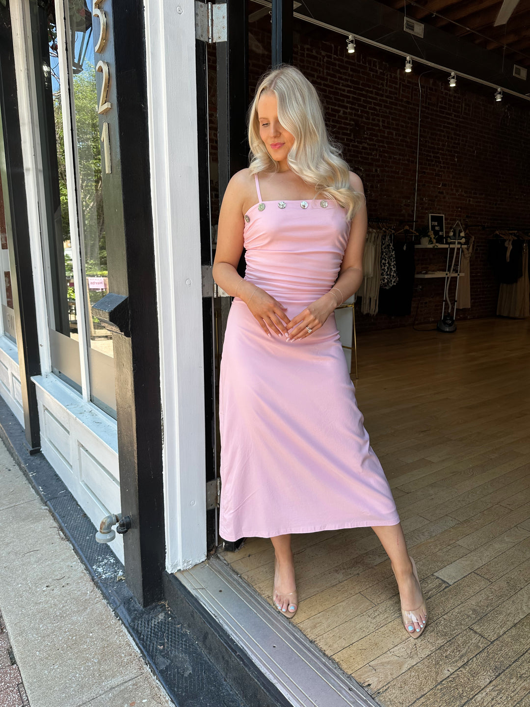 Woman wearing light pink midi dress with ruched sides, adjustable straps, and shell button detailing. 