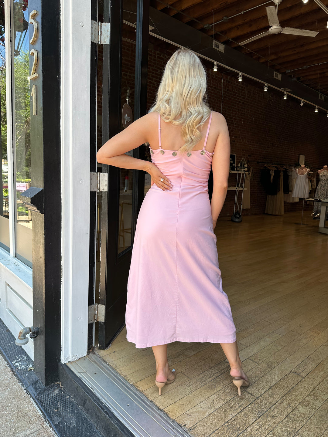 Woman wearing light pink midi dress with ruched sides, adjustable straps, and shell button detailing. 