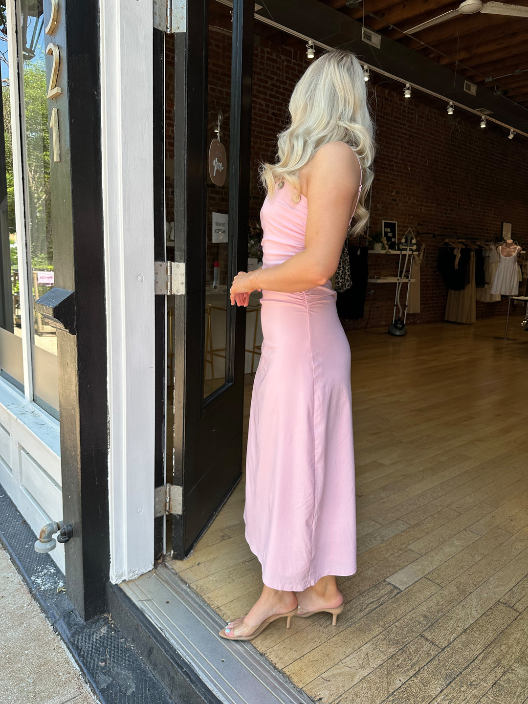 Woman wearing light pink midi dress with ruched sides, adjustable straps, and shell button detailing. 