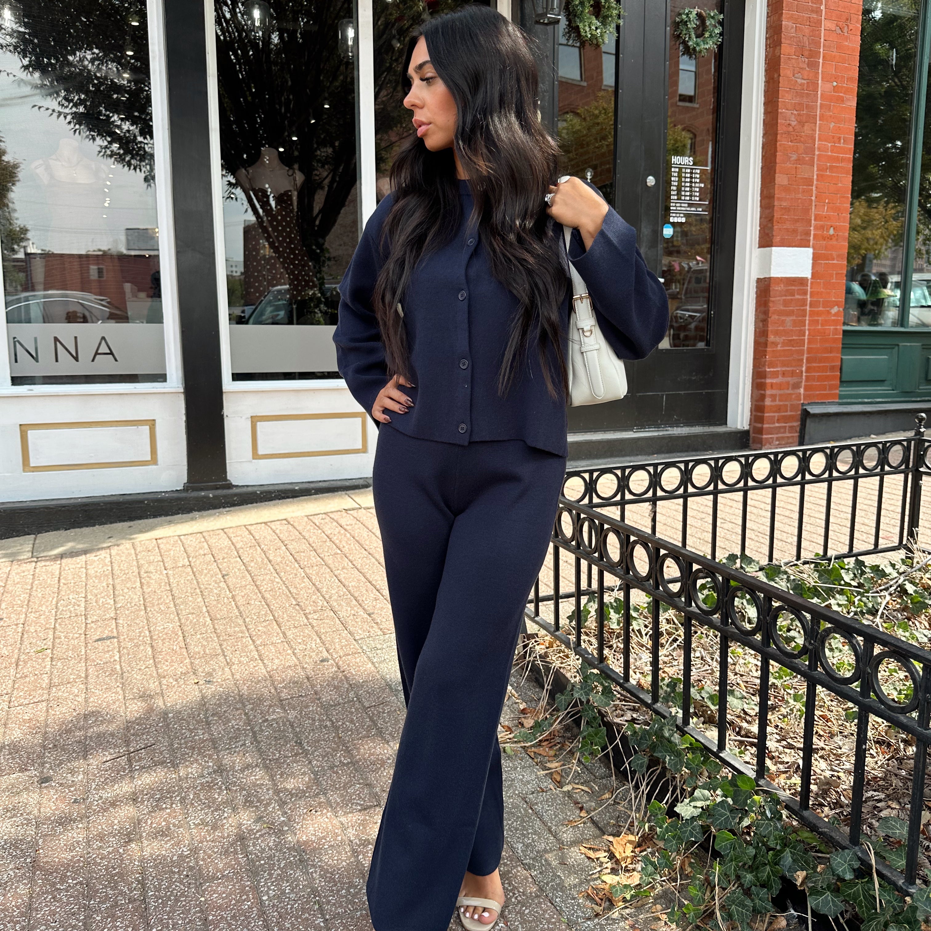 Woman wearing navy blue knit two piece set with button down cardigan and wide leg pant. 