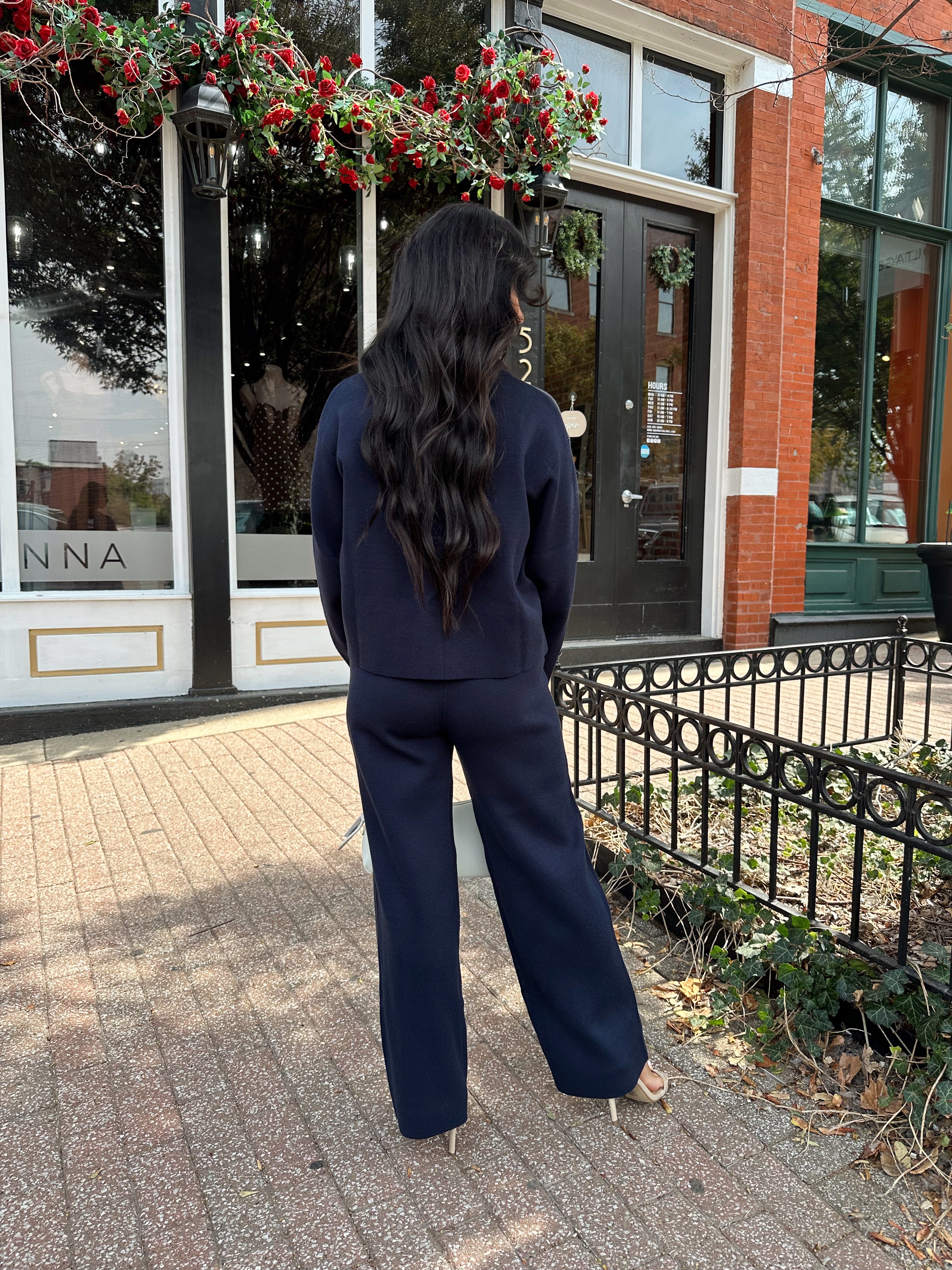 Woman wearing navy blue knit two piece set with button down cardigan and wide leg pant. 