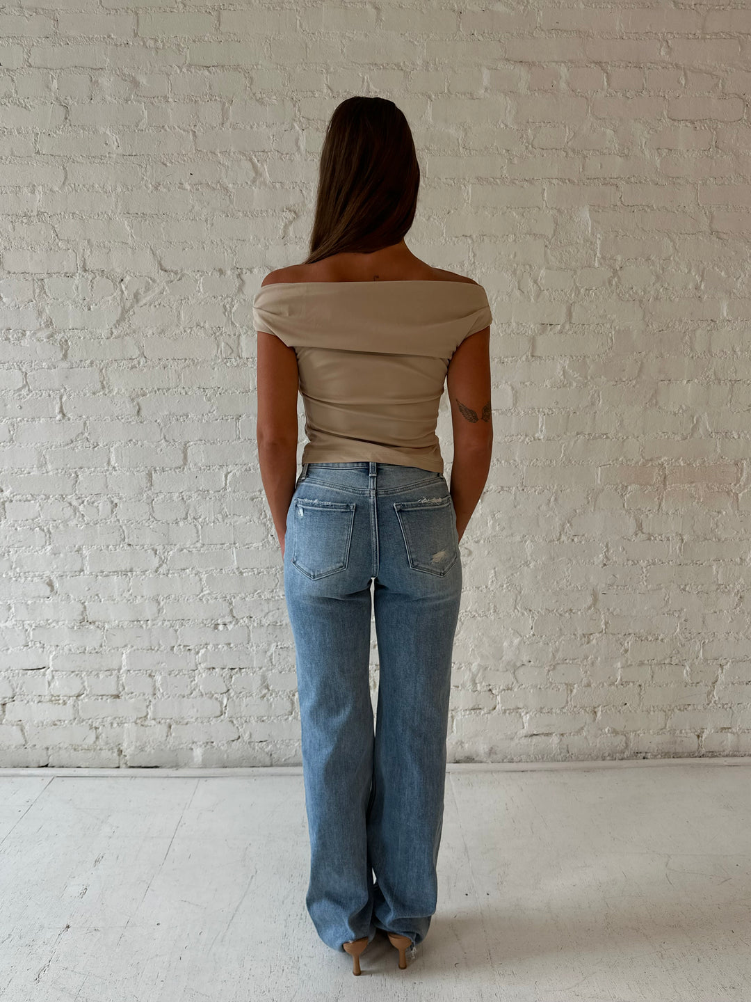 Woman wearing high waisted distressed jeans with brown tube top.