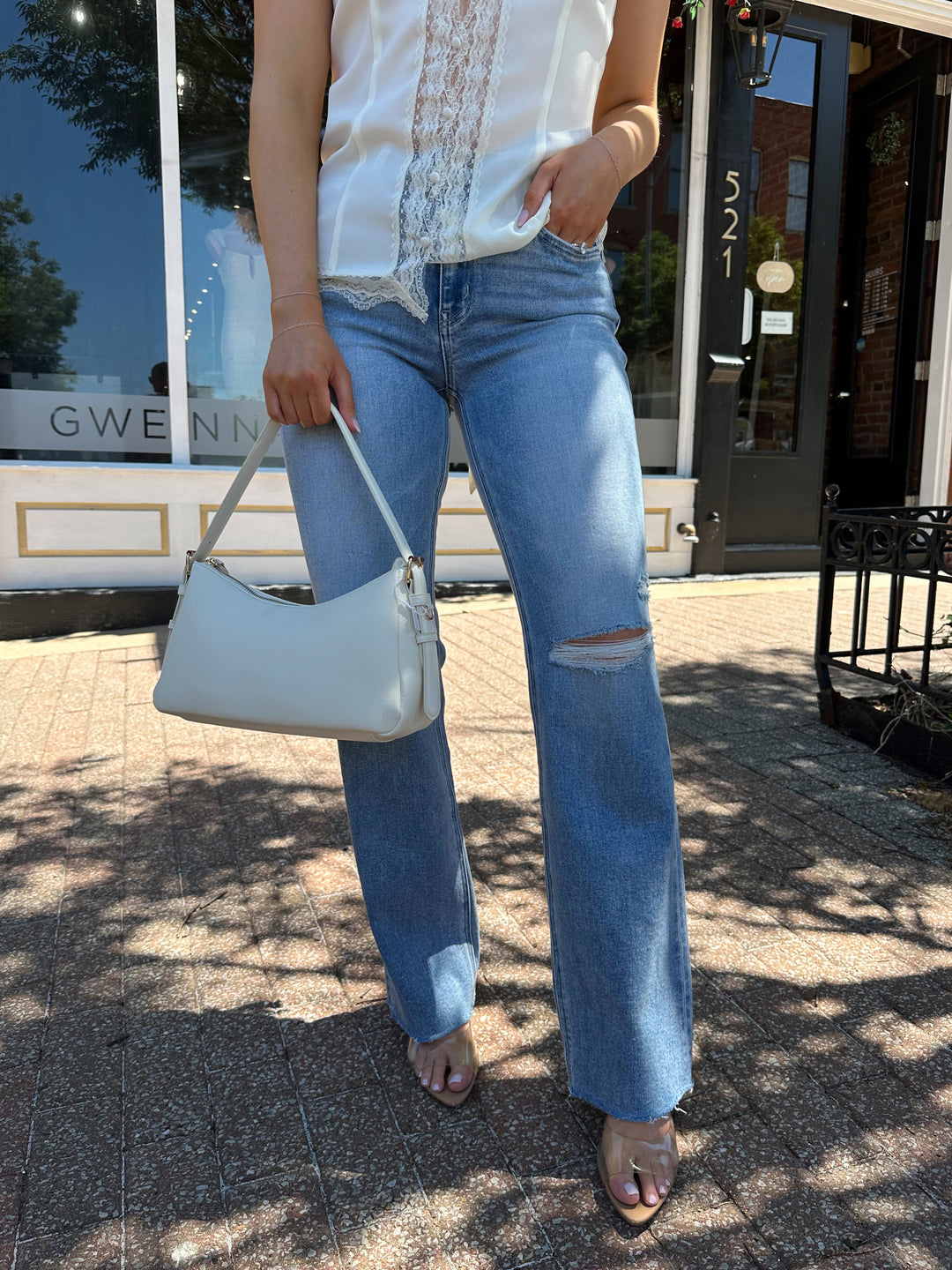 Woman wearing medium wash high rise jean with a slim wide leg fit, and slight distressing.